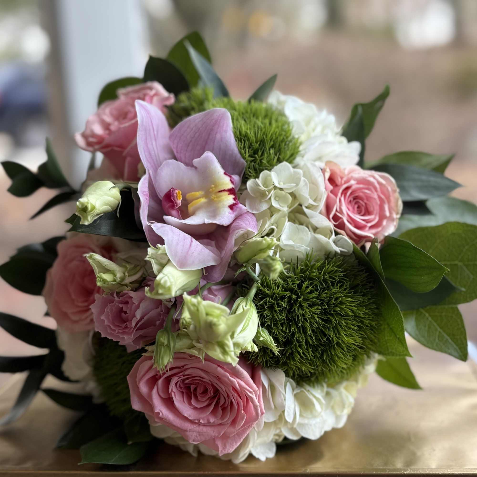 Round bouquet of pink roses, pink orchid, white hydrangea, and green mossy accent blooms