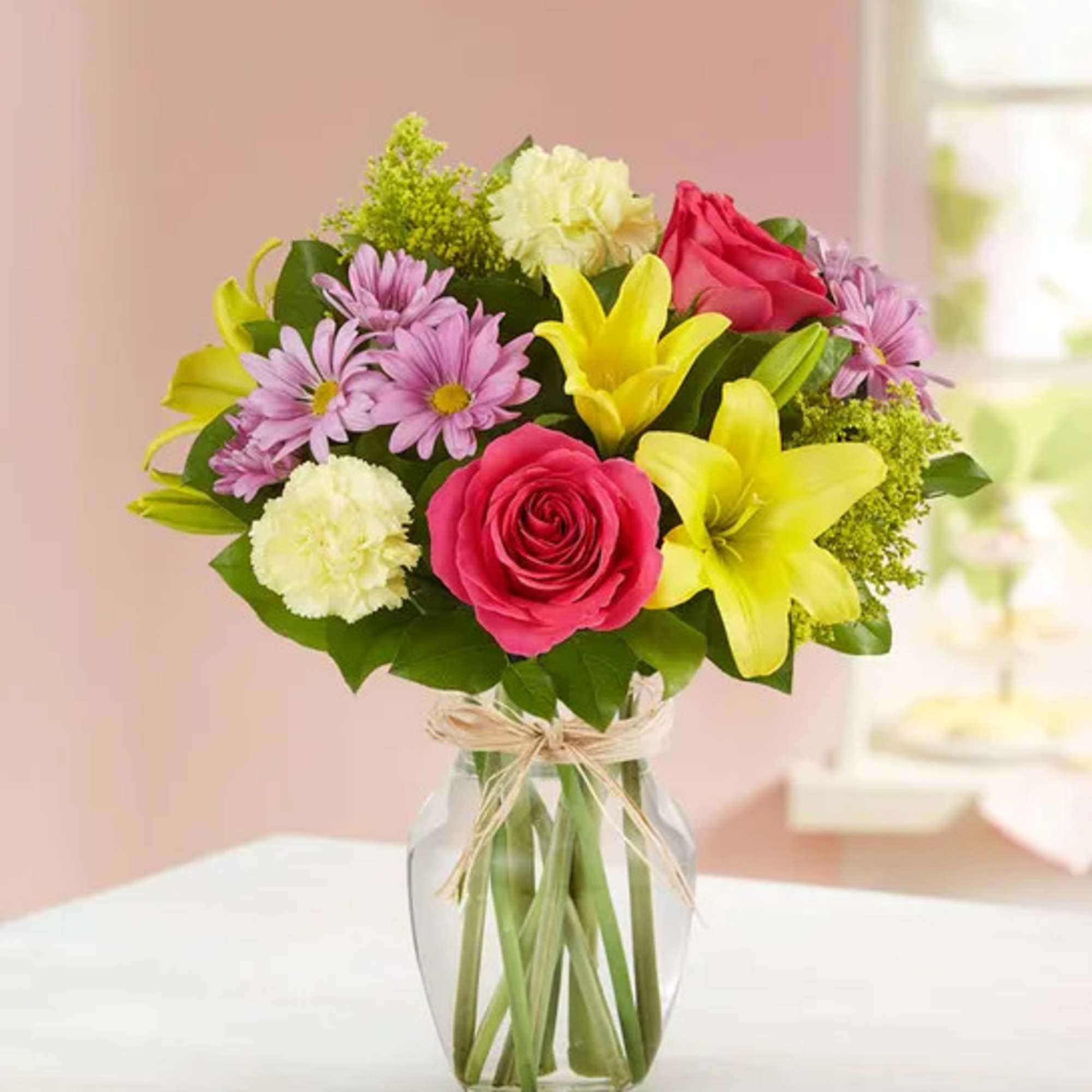 Bouquet of pink roses, yellow lilies, and purple daisies in a glass vase