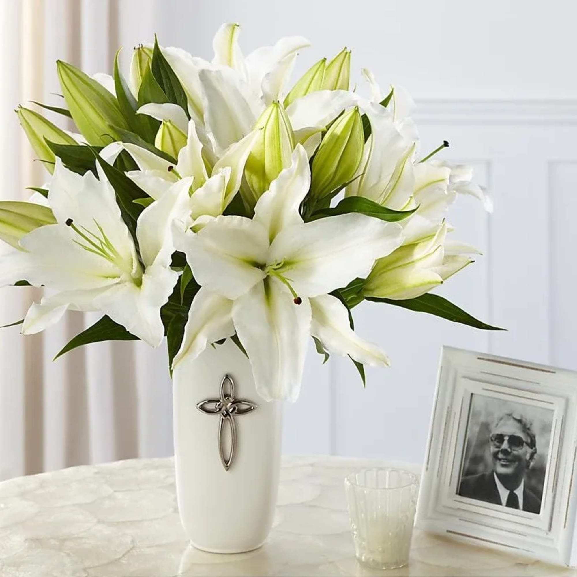 White lilies arranged in a tall vase with a cross emblem