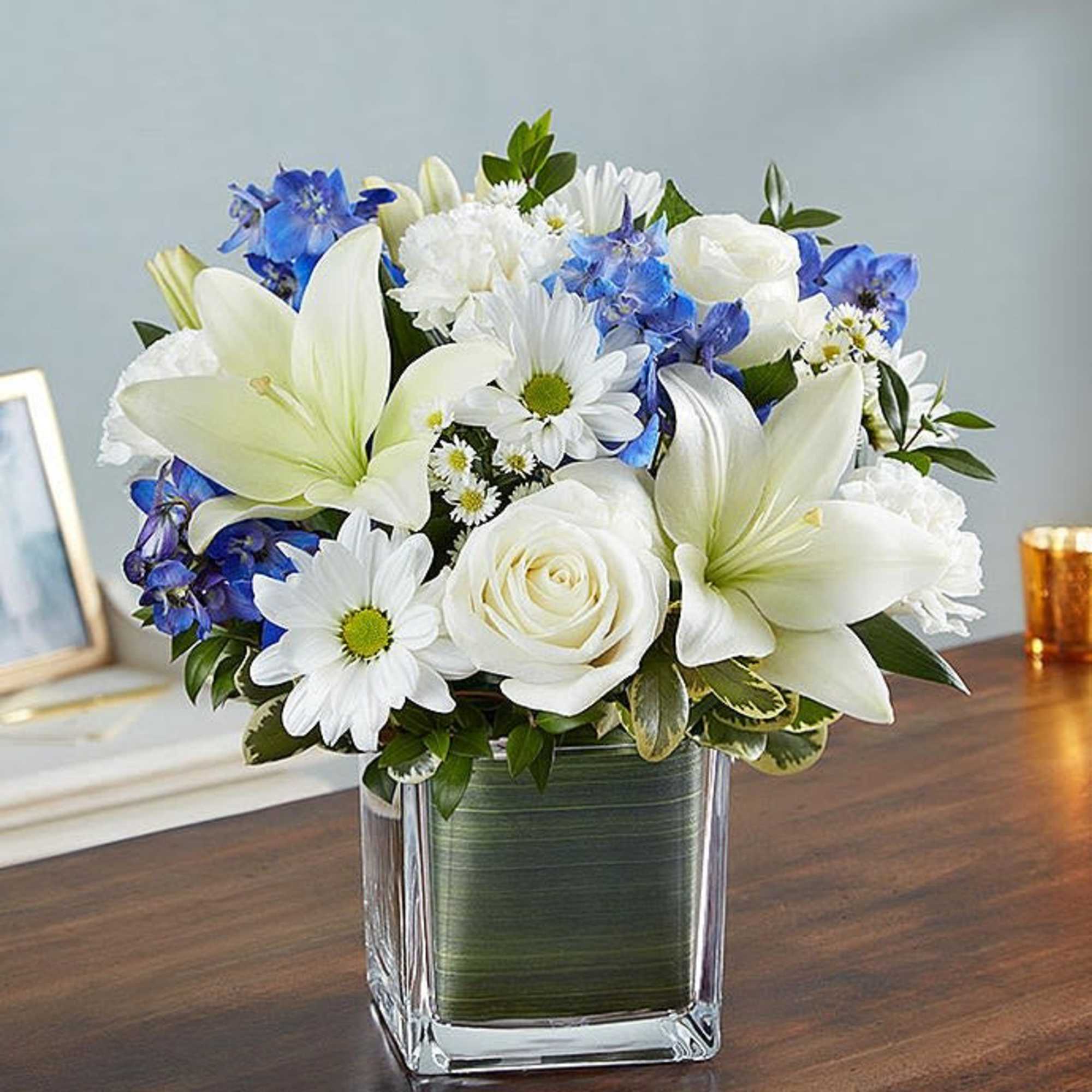 White lilies, roses, and blue flowers in a square glass vase