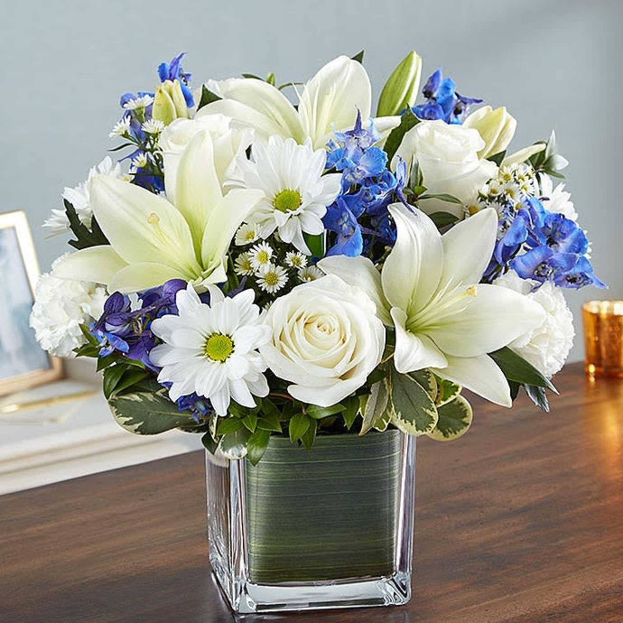 White lilies, roses, and daisies in a square glass vase