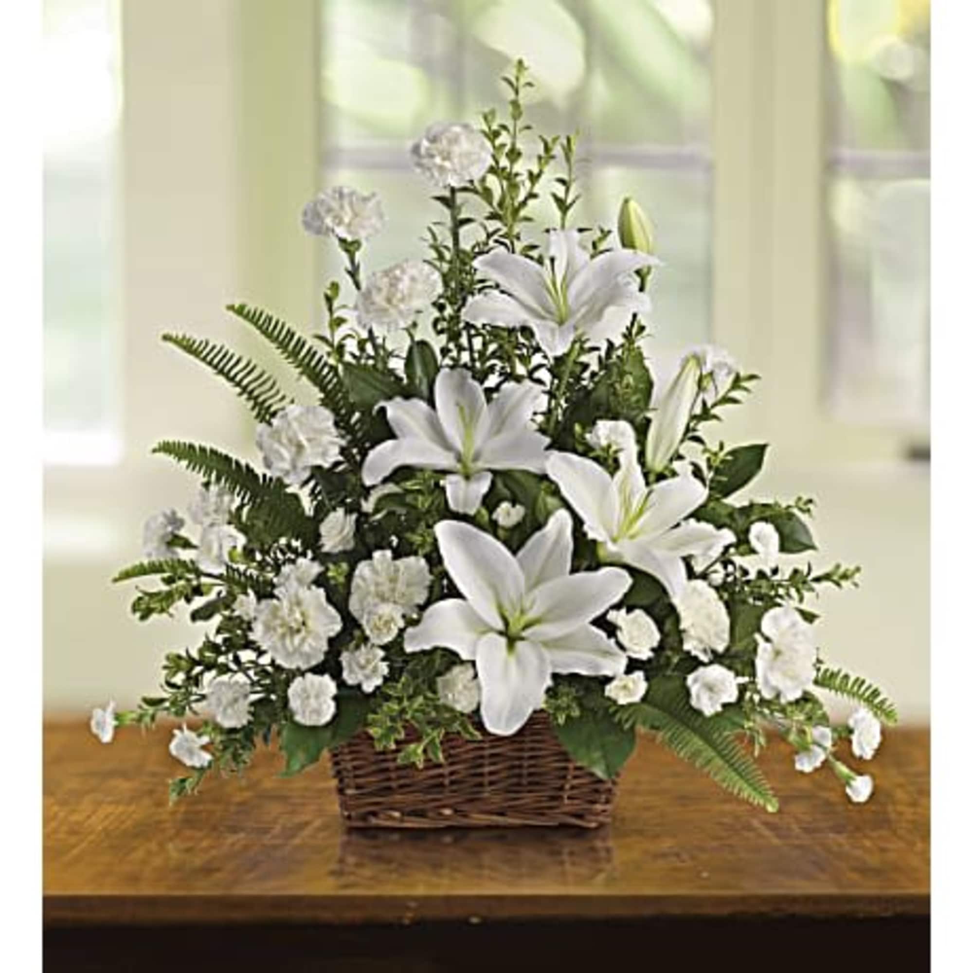 White lilies and carnations in a wicker basket arrangement on a wooden table