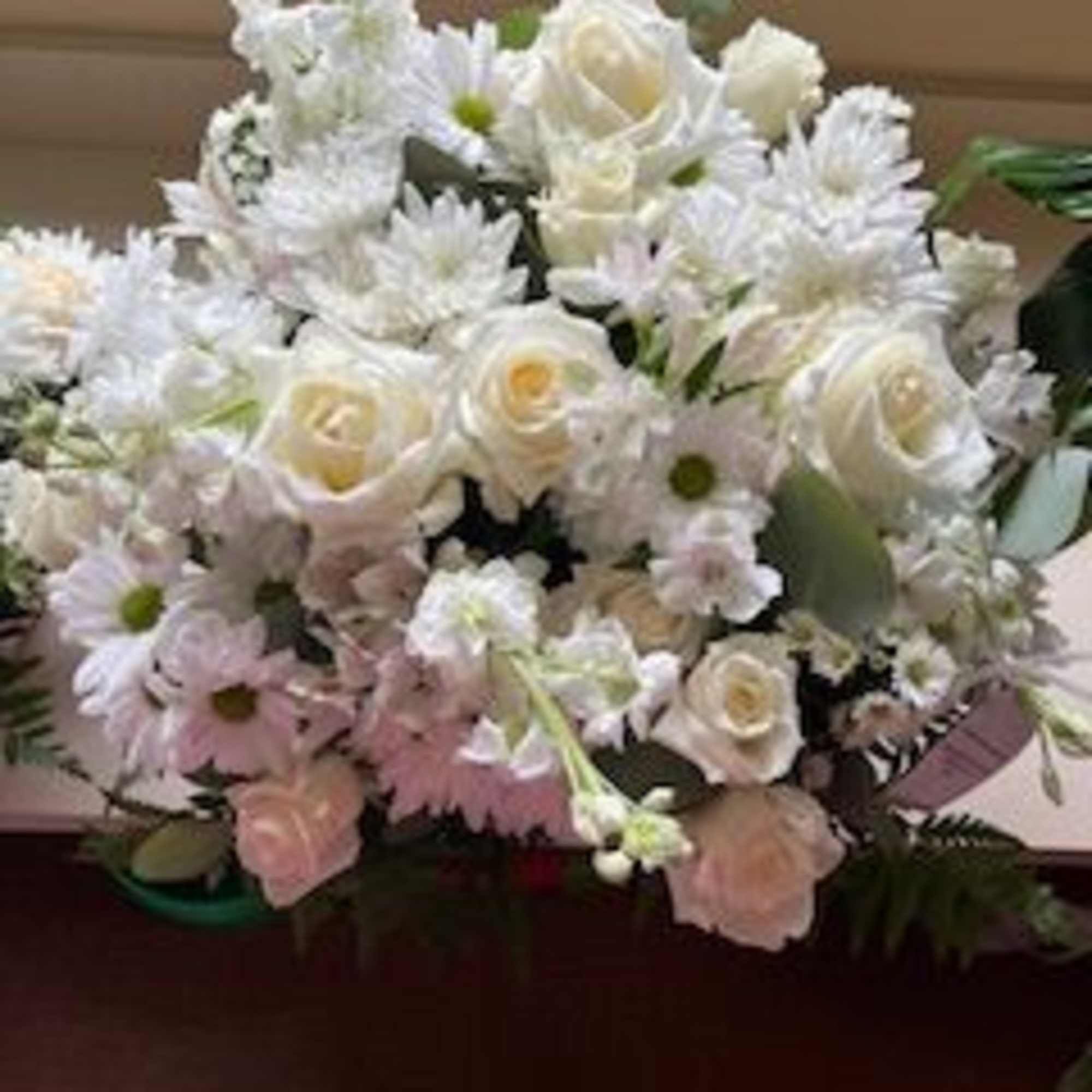 White arrangement of roses, daisies, and other blooms in a low container