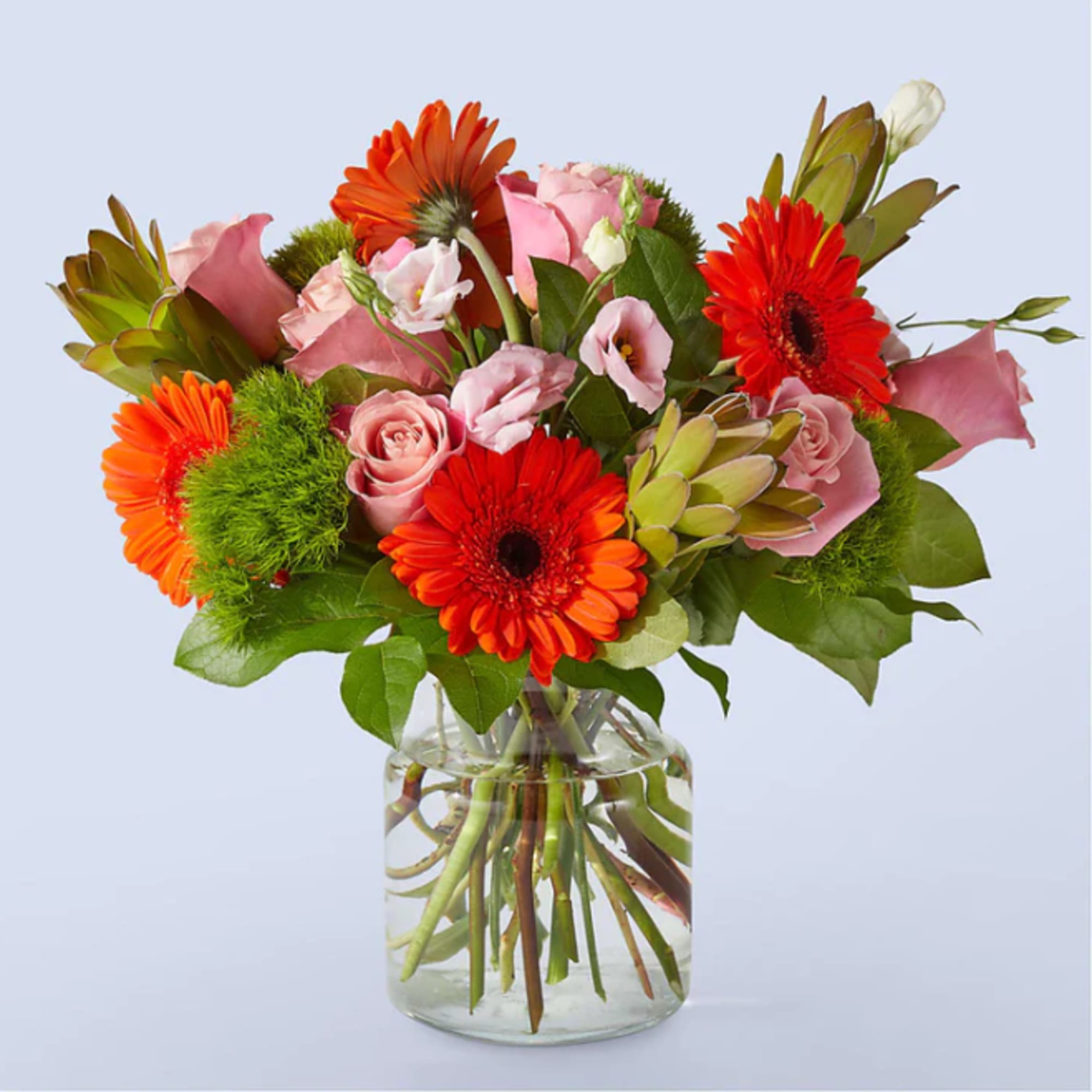 Pink roses and orange gerbera daisies in a clear glass vase
