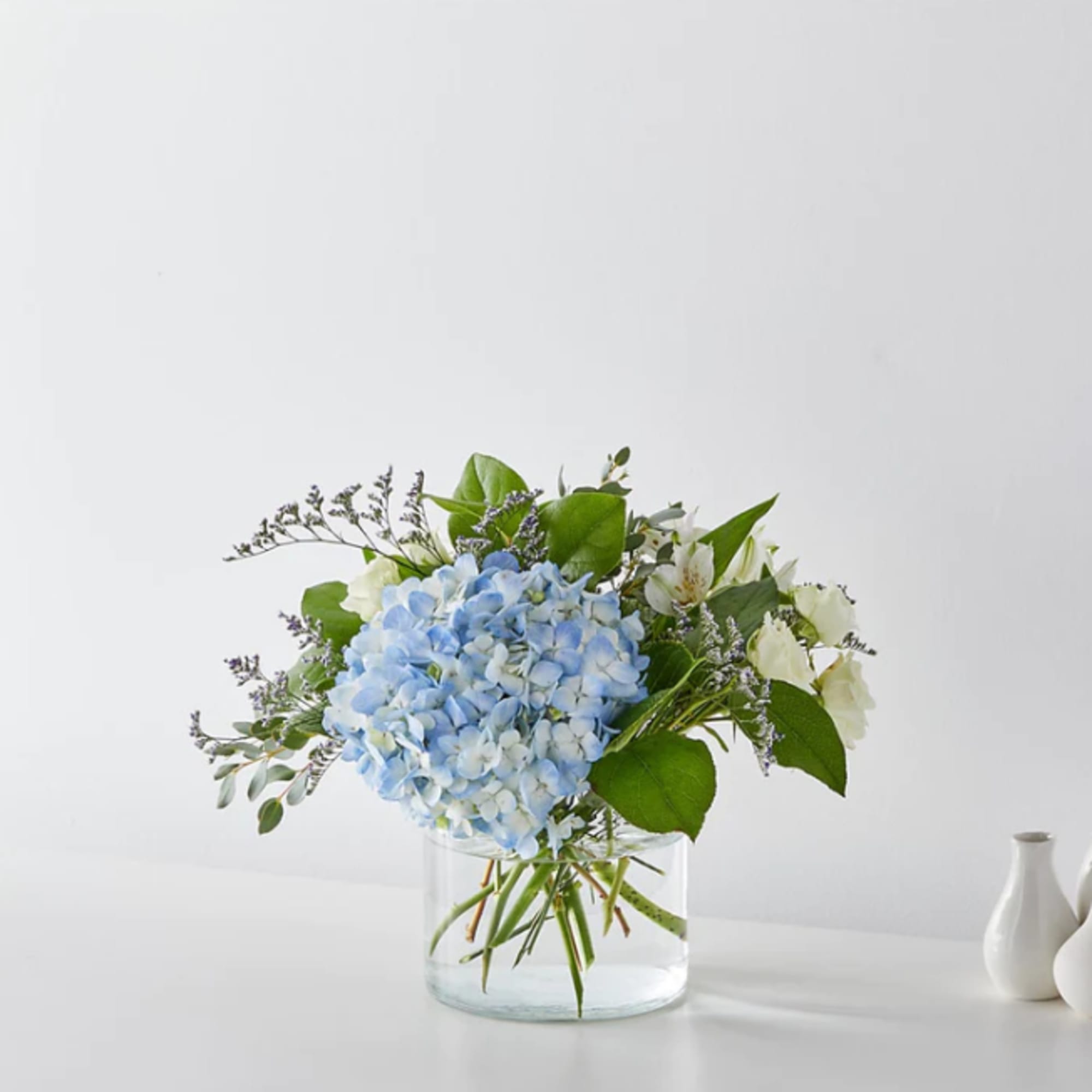 Blue hydrangea bouquet in a clear glass vase with white blooms