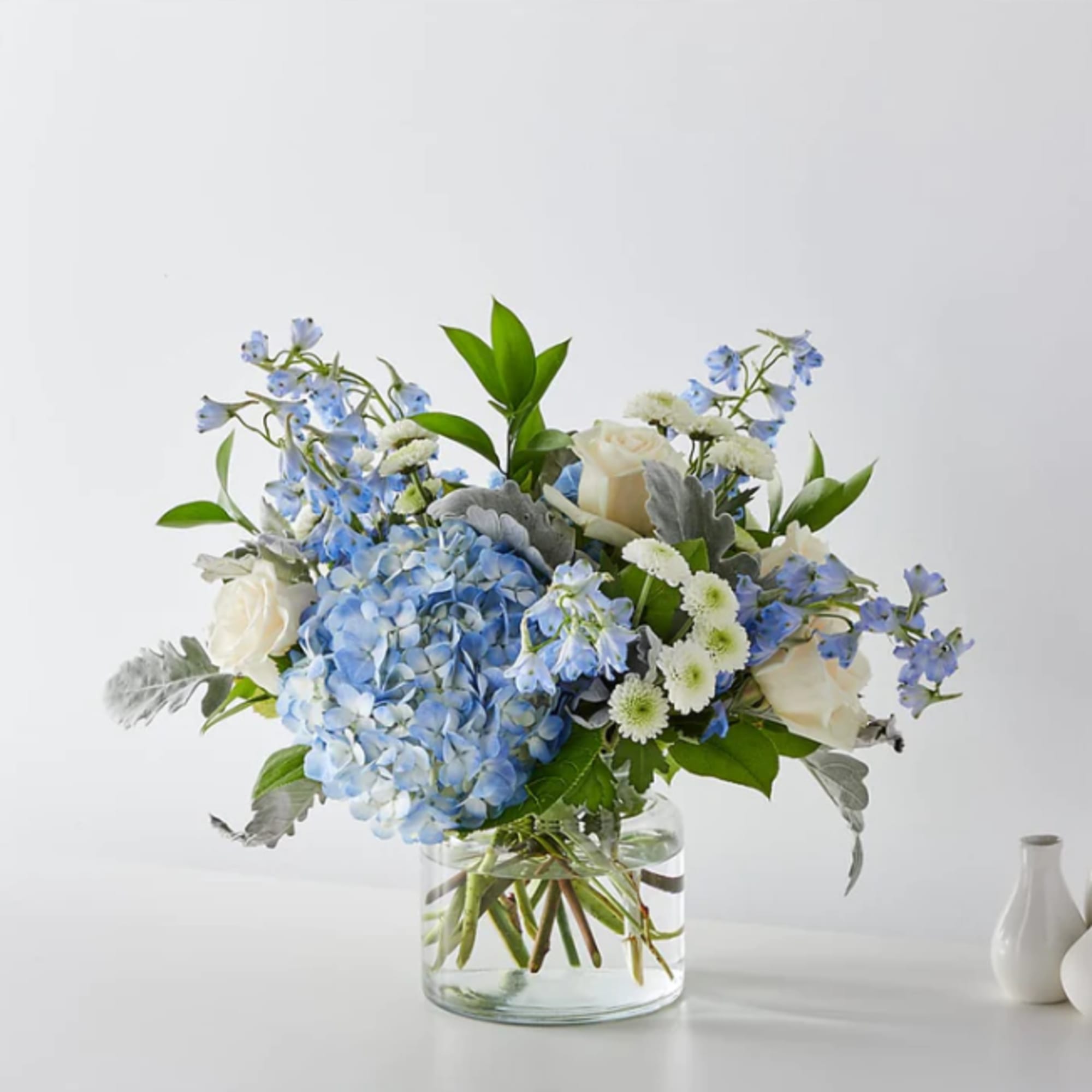 Blue hydrangeas and white roses in a clear glass vase