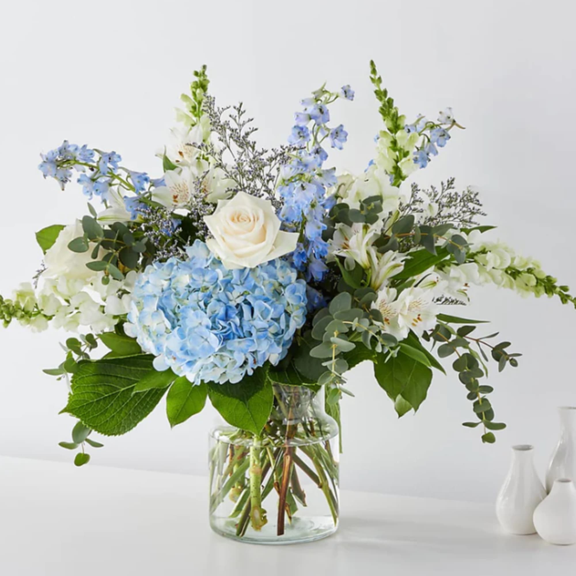 Blue hydrangea and white rose arrangement in a glass vase