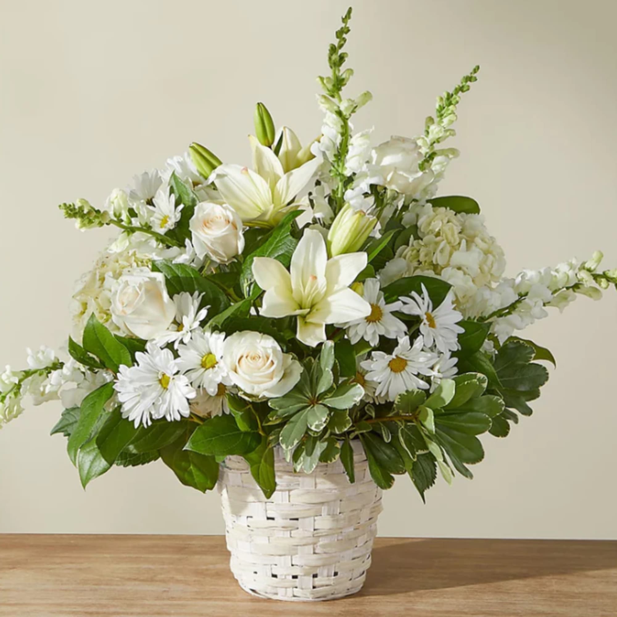 White lilies, roses, and daisies arranged in a white basket