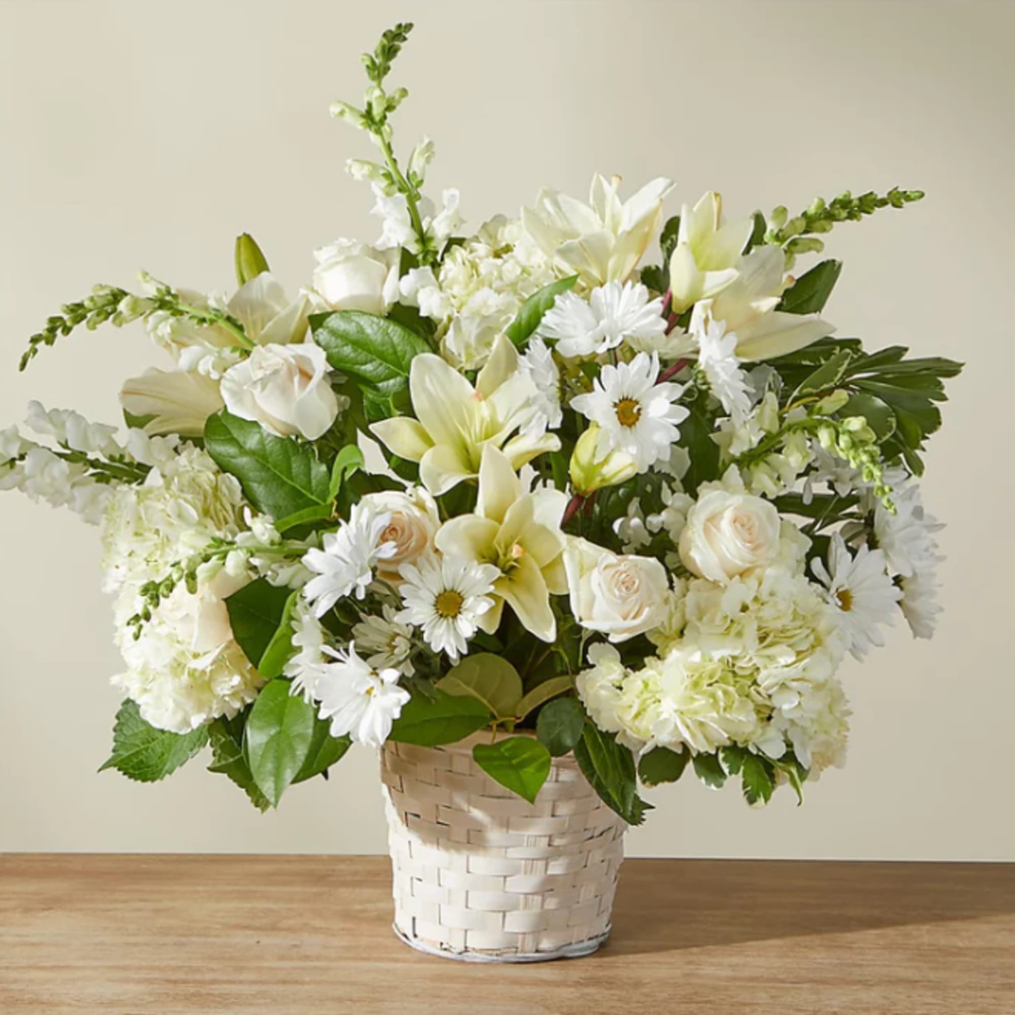White floral arrangement in a woven basket with roses, lilies, and daisies
