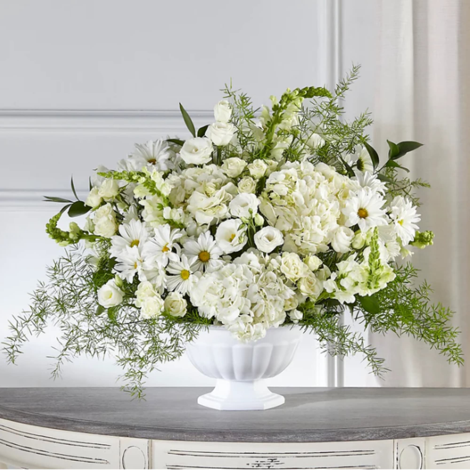 White floral arrangement in a white pedestal vase with daisies and roses