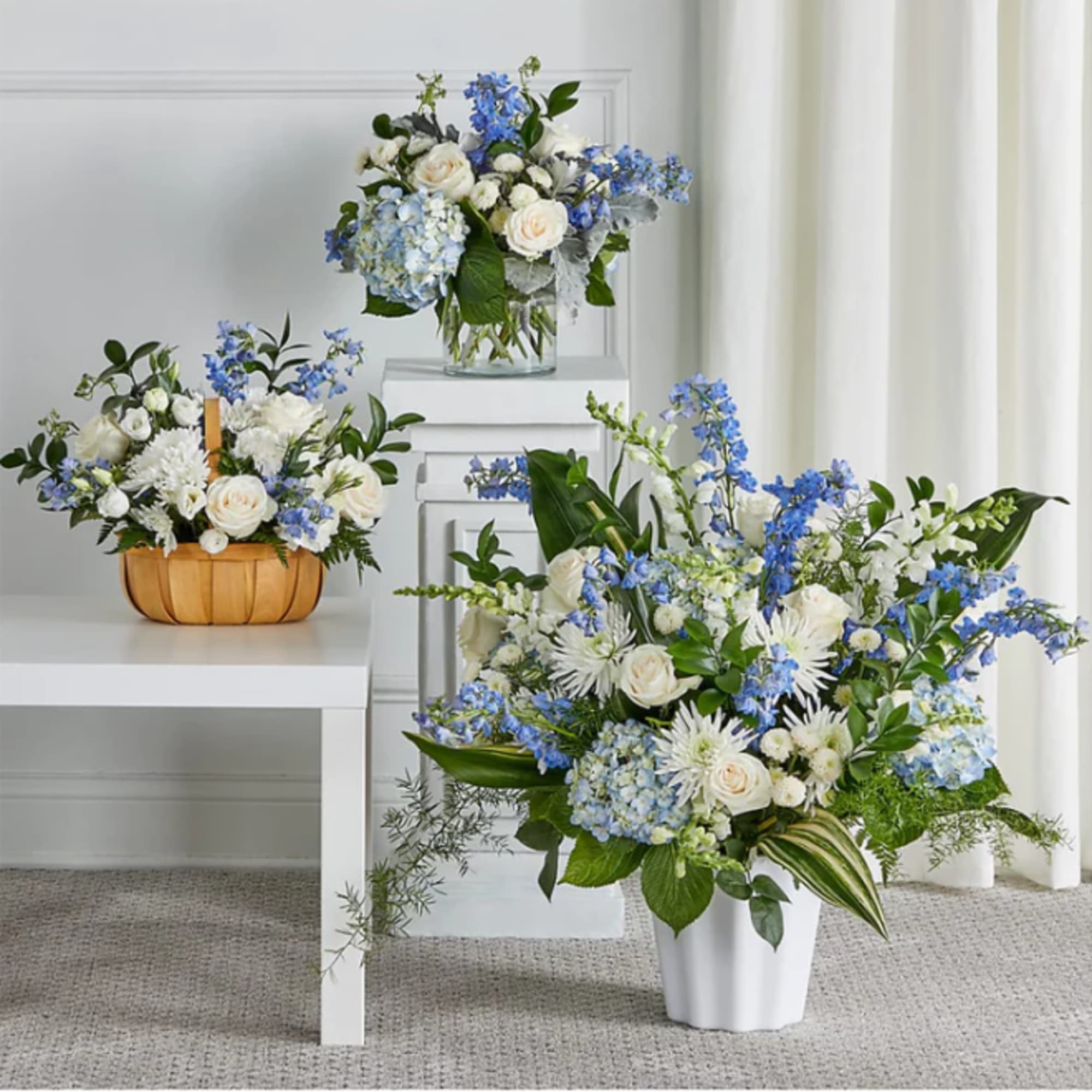Three blue and white floral arrangements in vases and a basket.