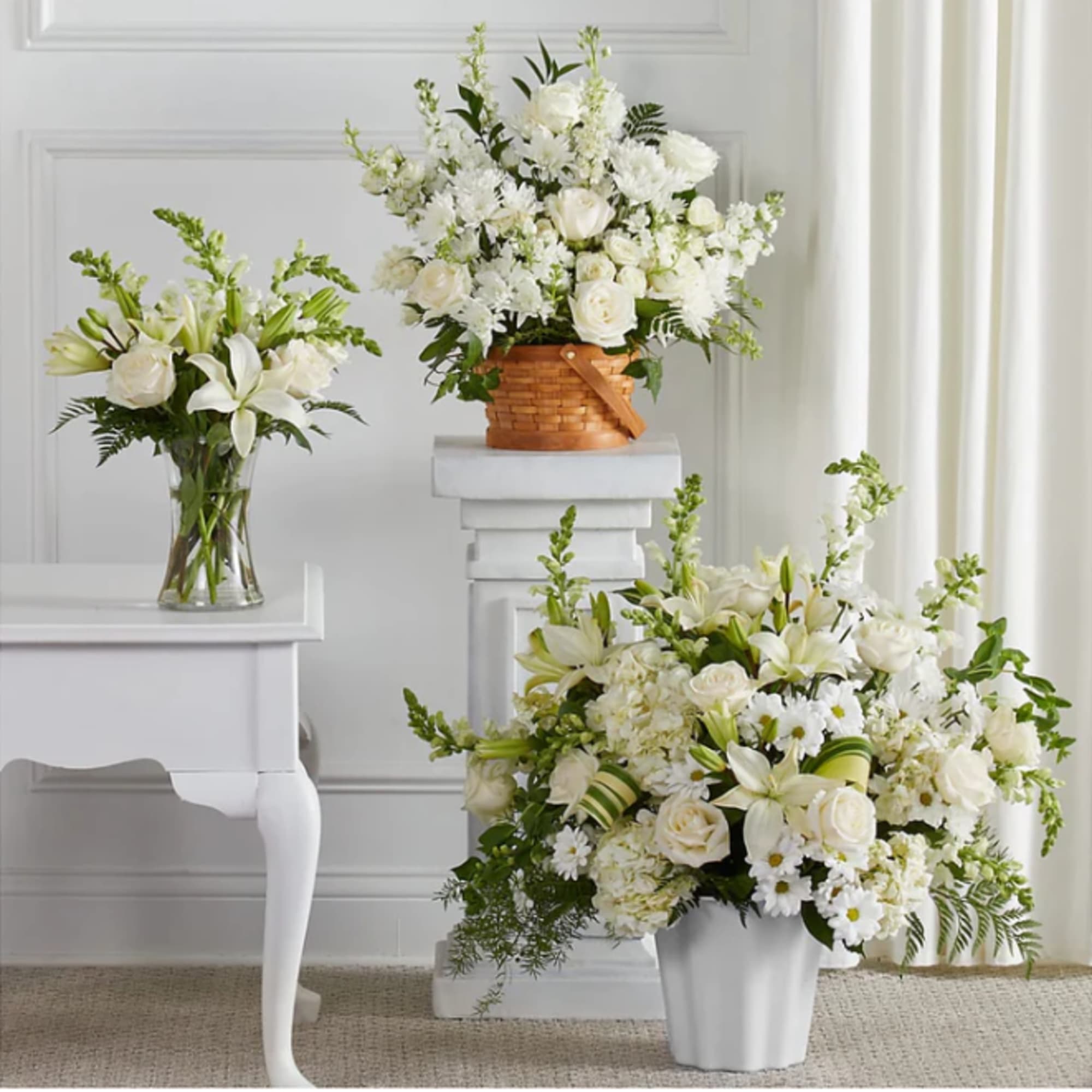 Three white floral arrangements in vases and a basket