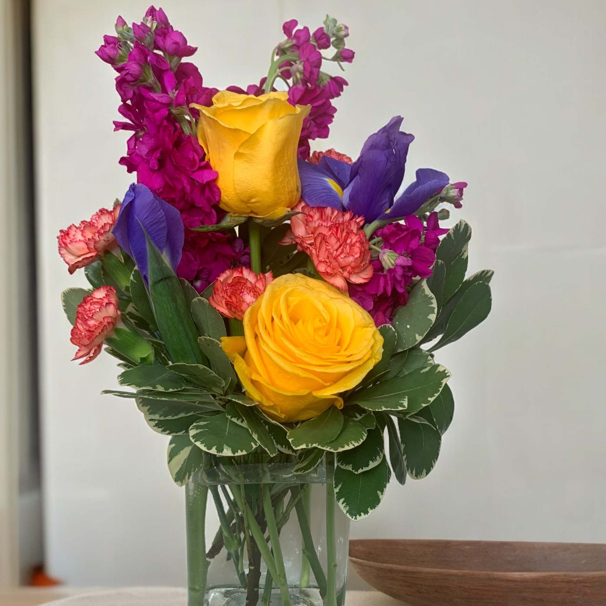 Colorful bouquet of yellow roses, purple irises, and pink flowers in a glass vase