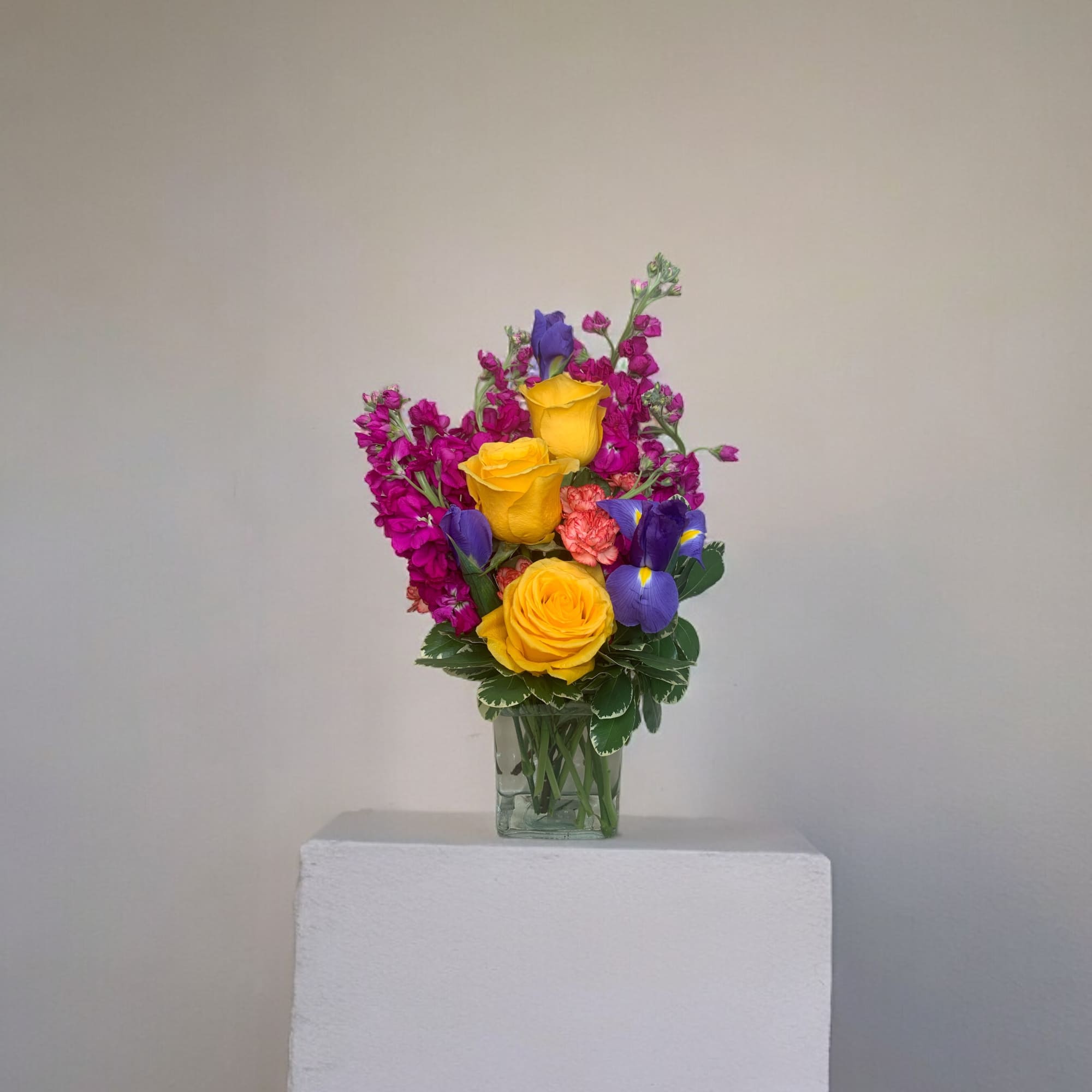 Colorful bouquet of yellow roses, purple irises, and magenta flowers in a glass vase
