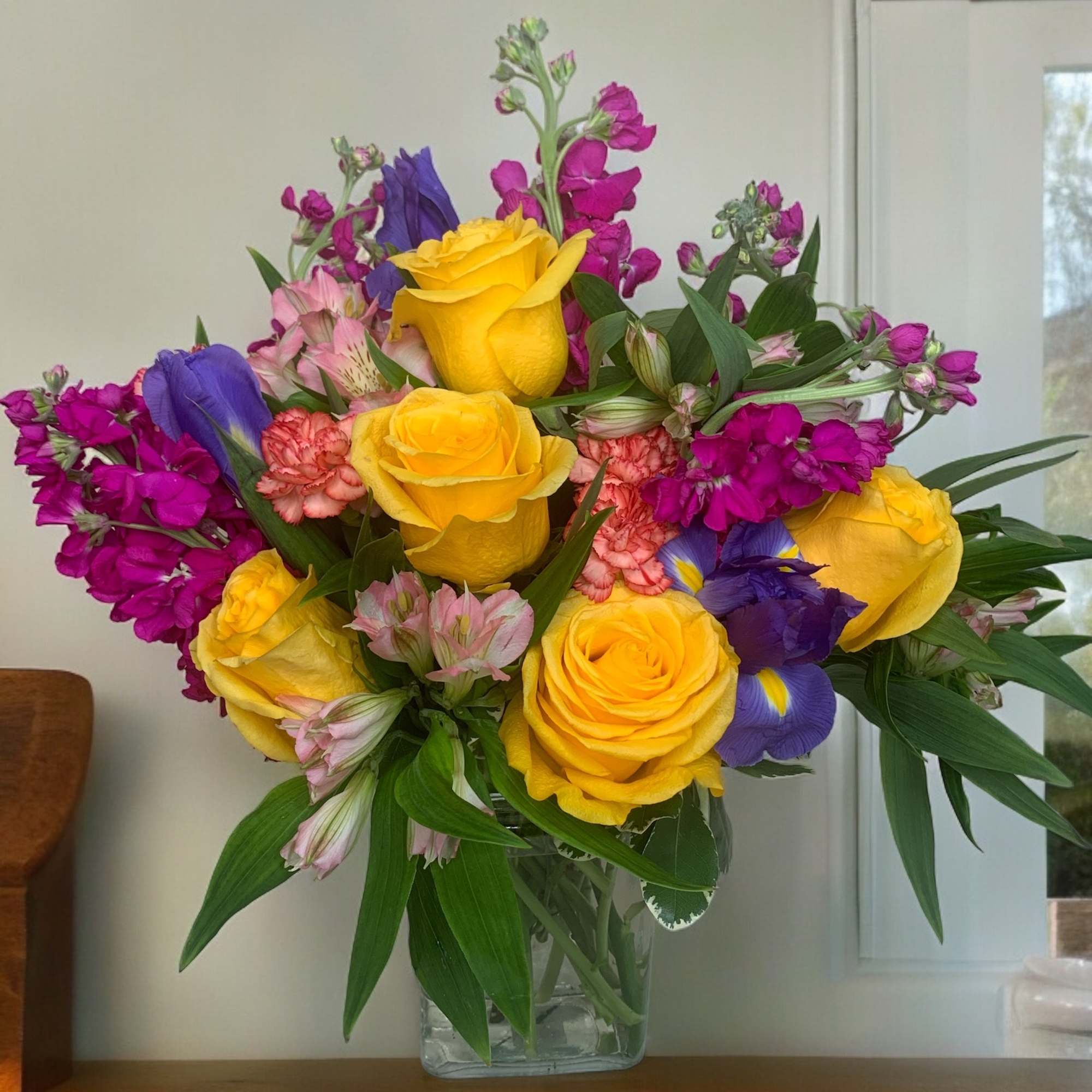Bouquet of yellow roses, purple irises, and pink flowers in a glass vase