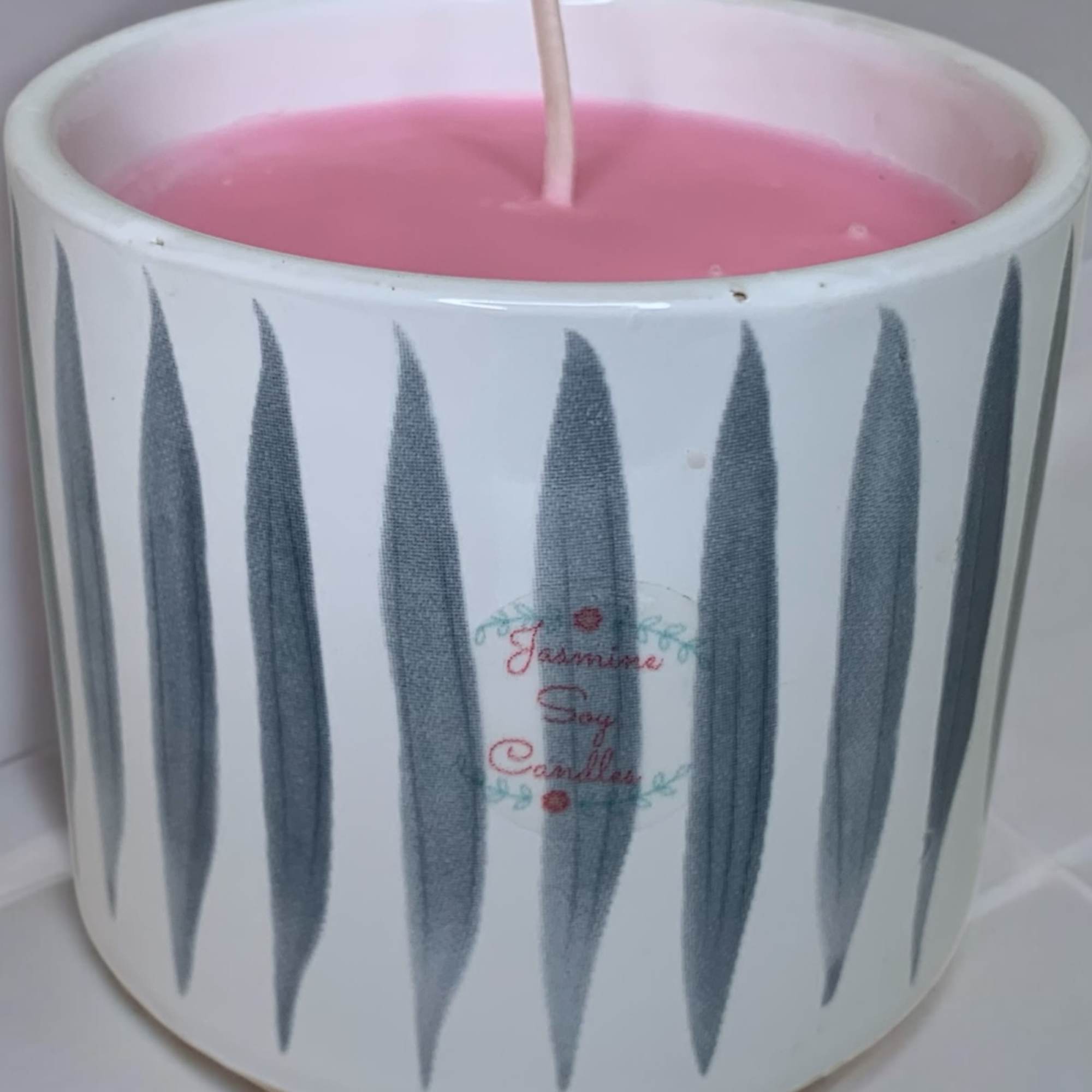 Pink candle in a white ceramic holder with a lit wick