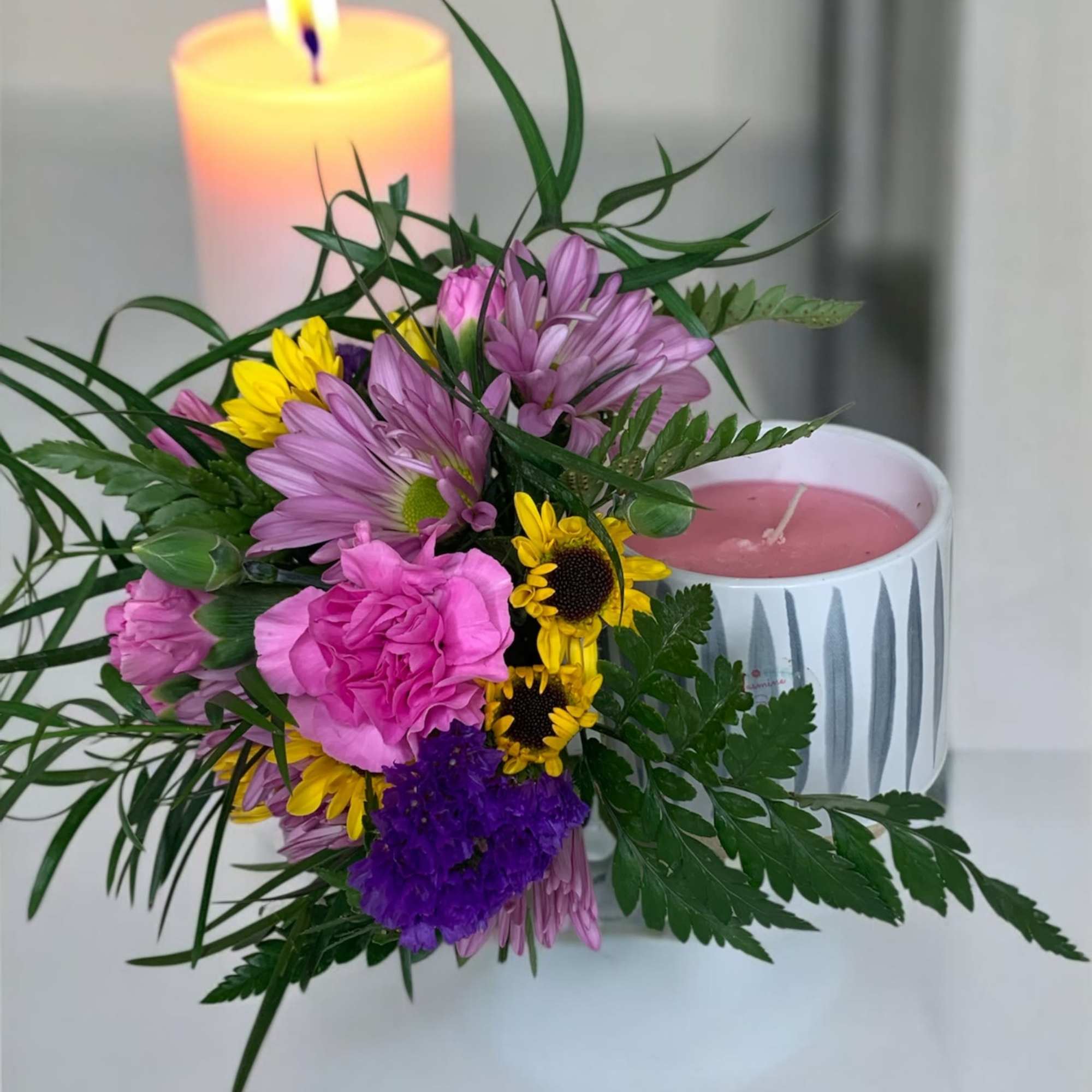 Bouquet with pink and yellow flowers beside two lit candles