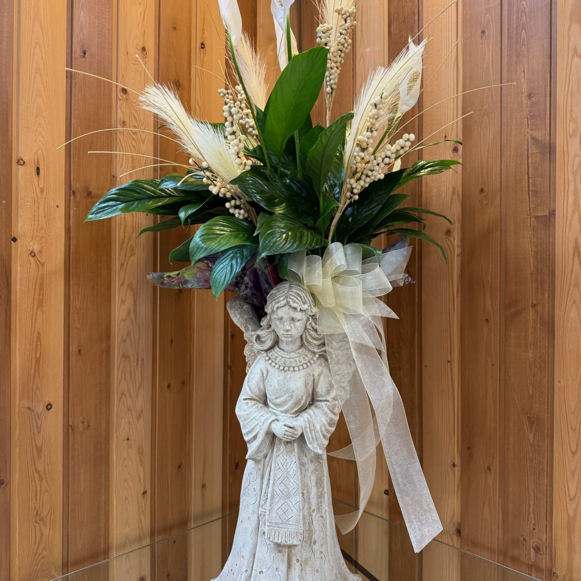 Floral arrangement on a stone angel statue with white ribbon