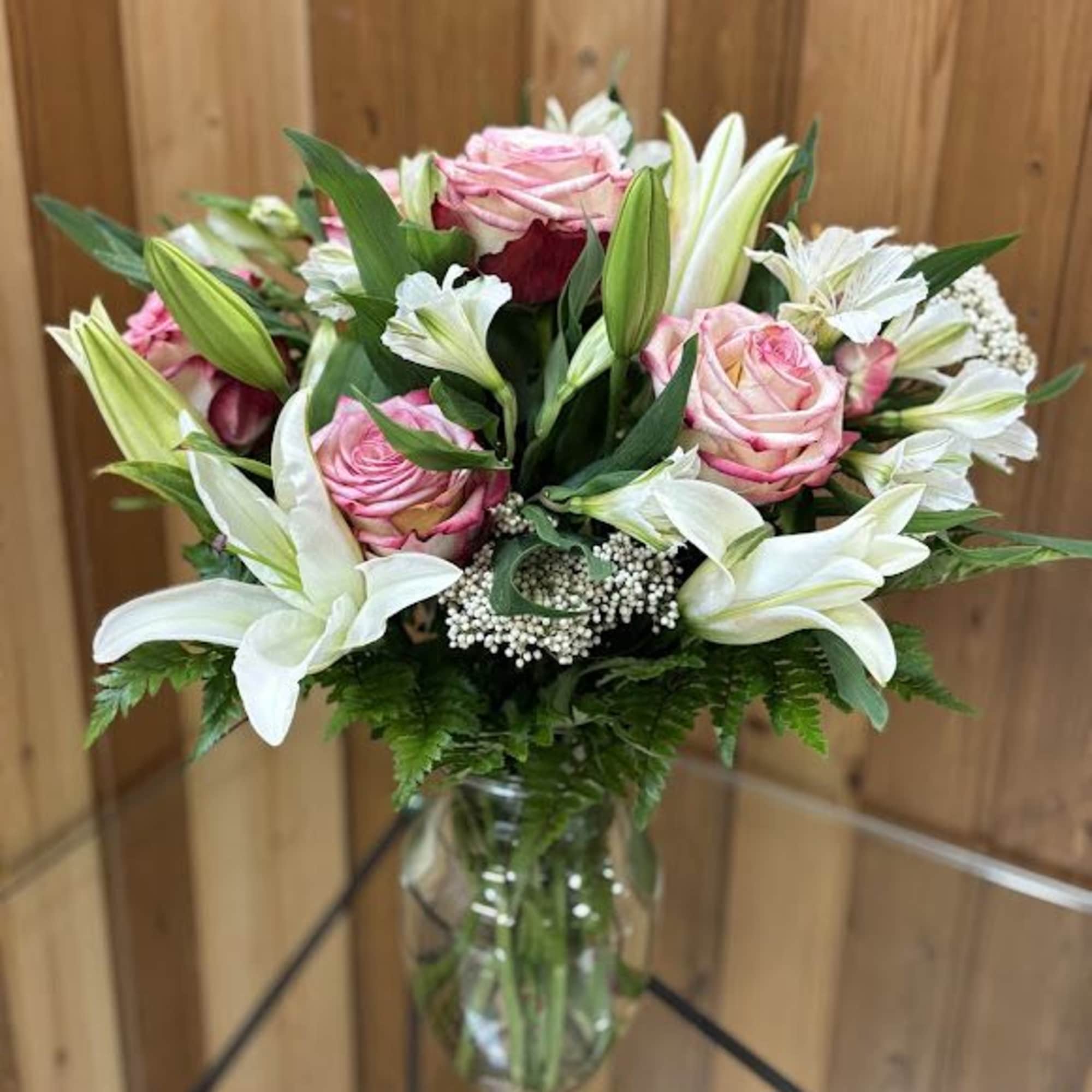 Mixed bouquet of pink roses and white lilies arranged in a clear glass vase.