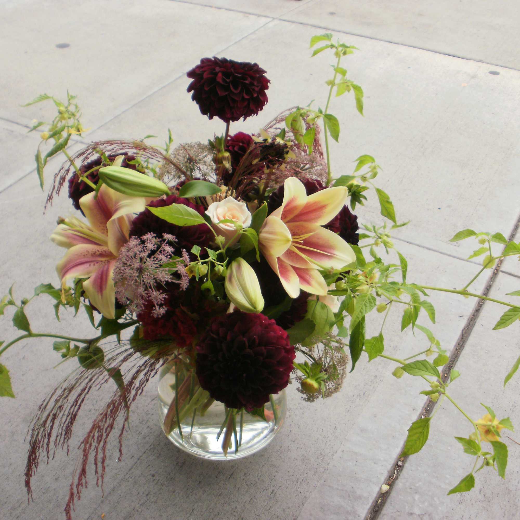 Low glass vase with burgundy dahlias and pink lilies with trailing greenery.