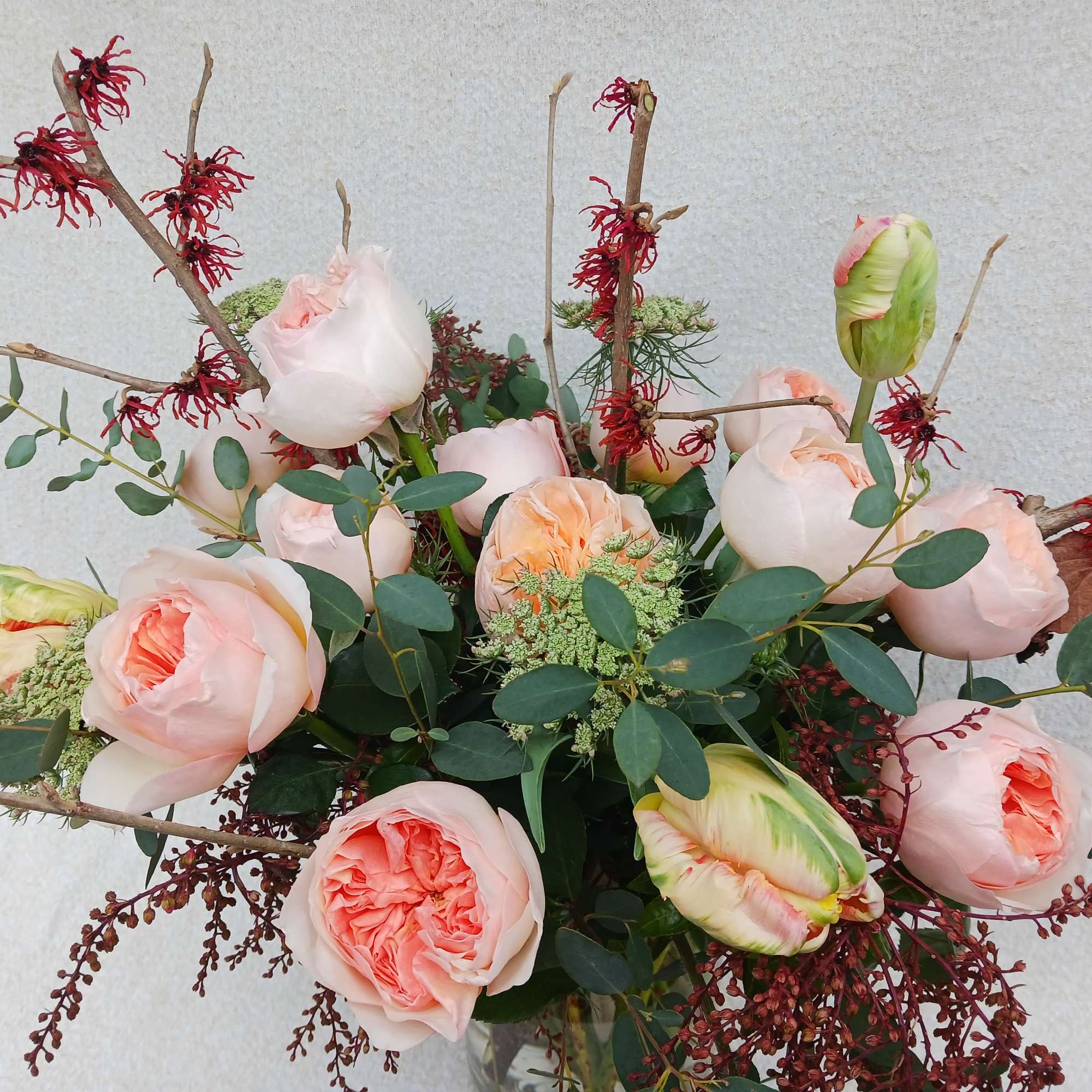 Loose arrangement of peach roses with green parrot tulips and red branching accents in a glass vase.