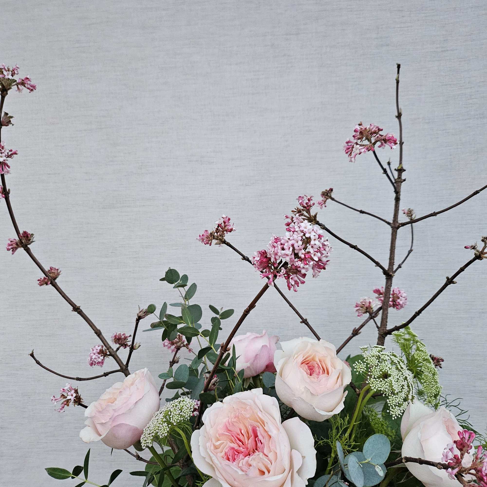 Tall arrangement with blush roses, white filler blooms, and branching stems with tiny pink flowers