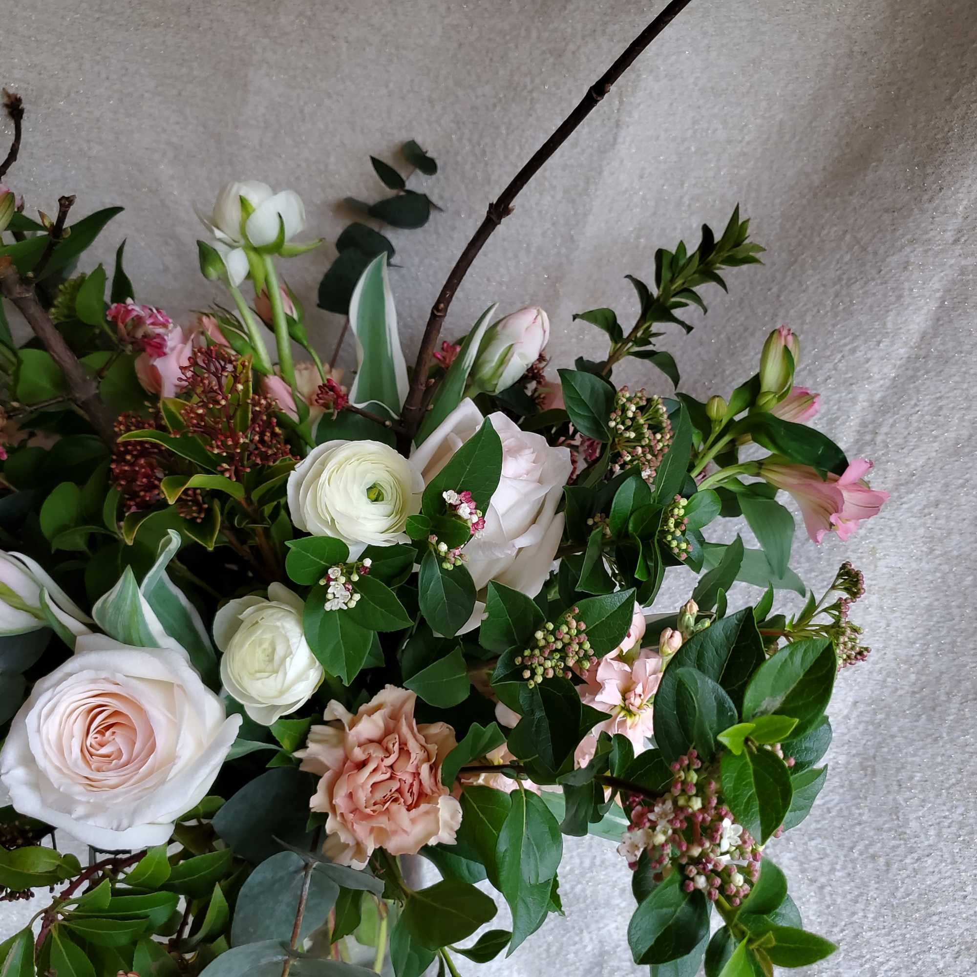 Loose arrangement of blush roses, white ranunculus, and pink flowers with branching accents