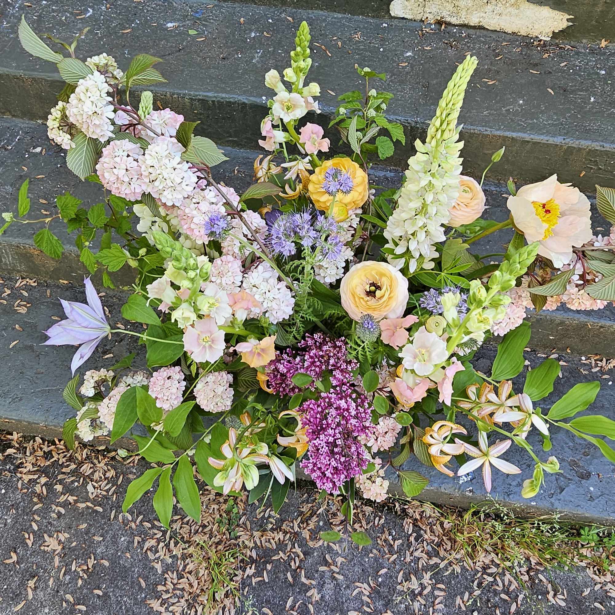 Loose garden-style arrangement of pastel flowers with purple accents displayed on outdoor stone steps