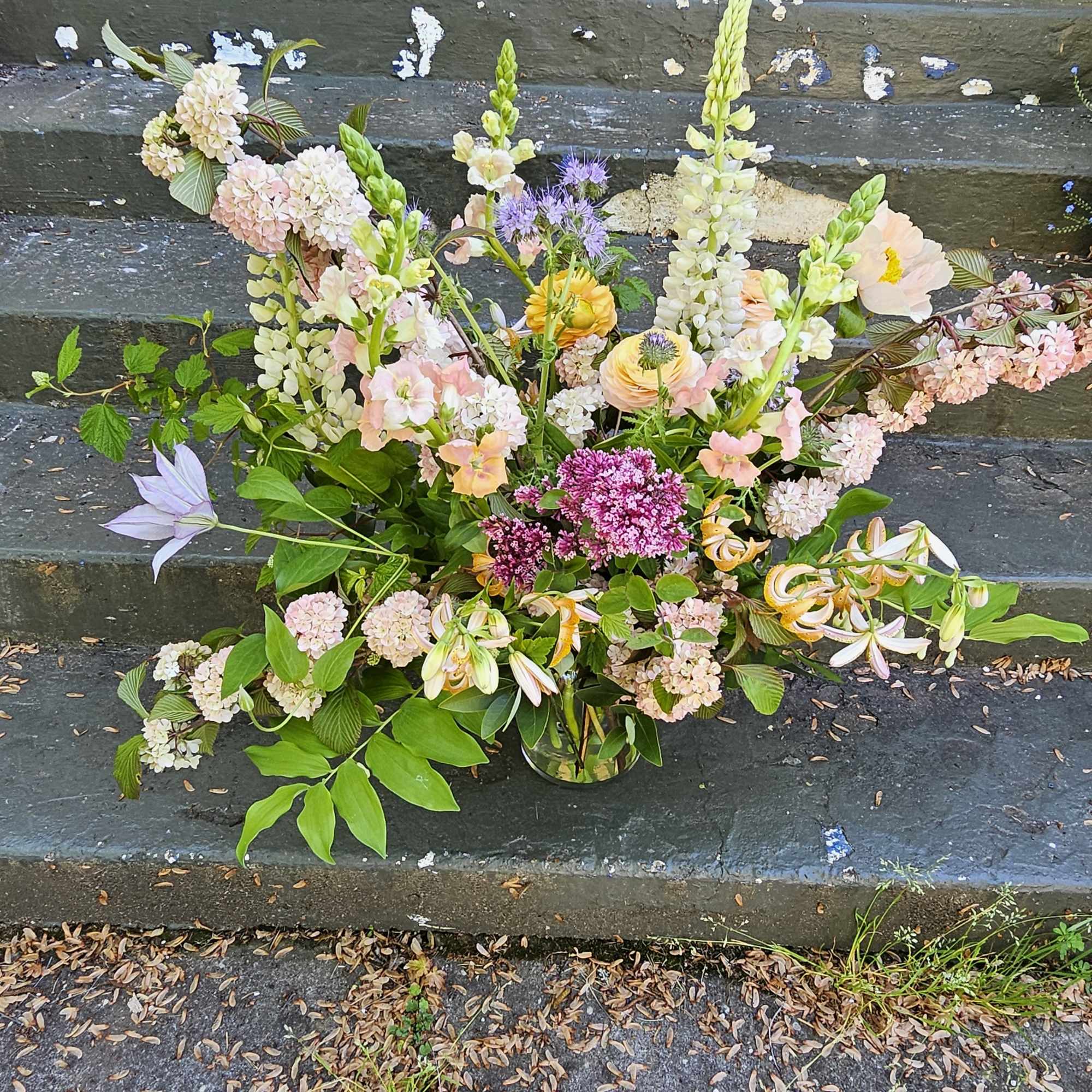Loose garden-style arrangement of pastel flowers with tall spires in a clear glass vase.