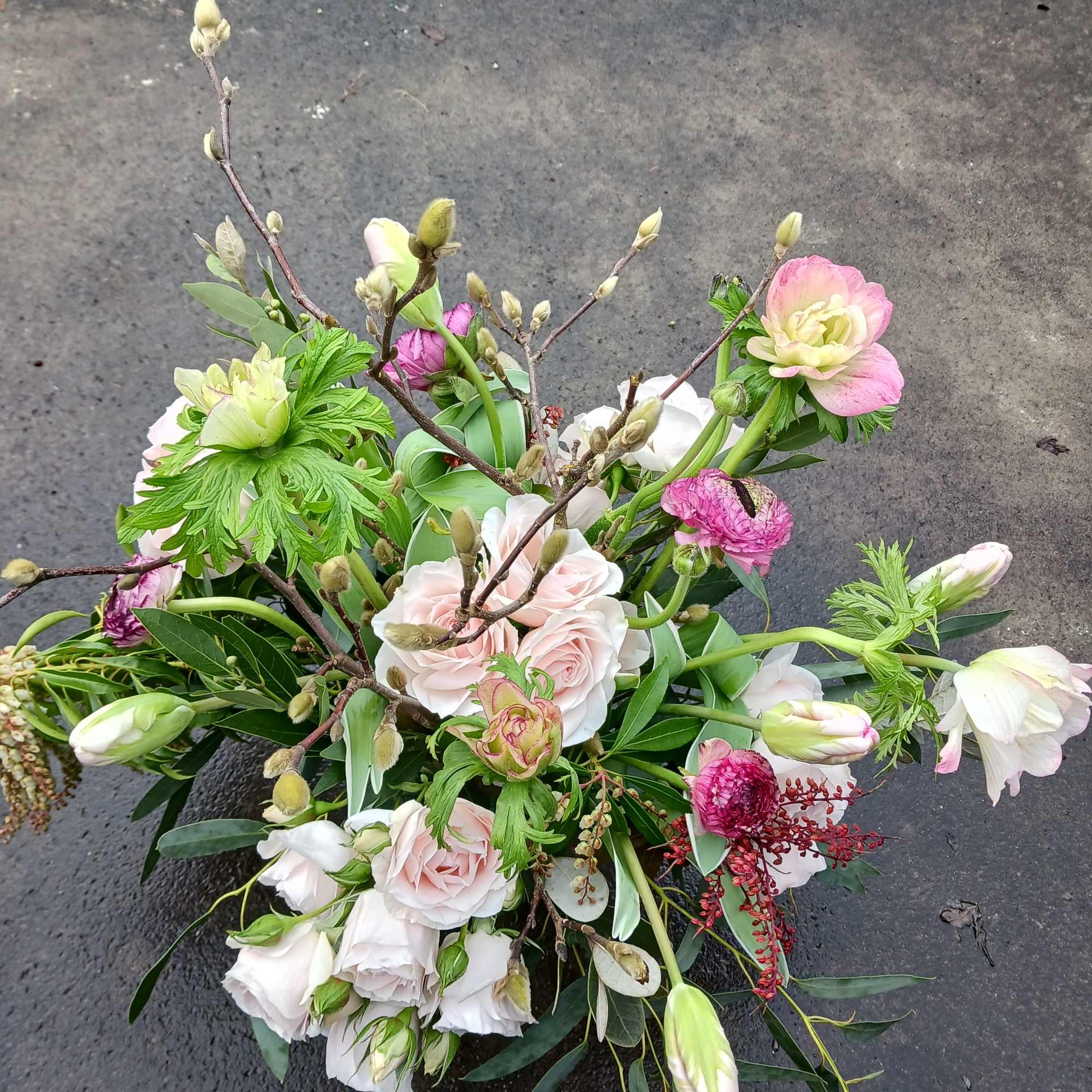 Loose garden-style arrangement of blush roses, pink ranunculus, and tulips with branching buds.