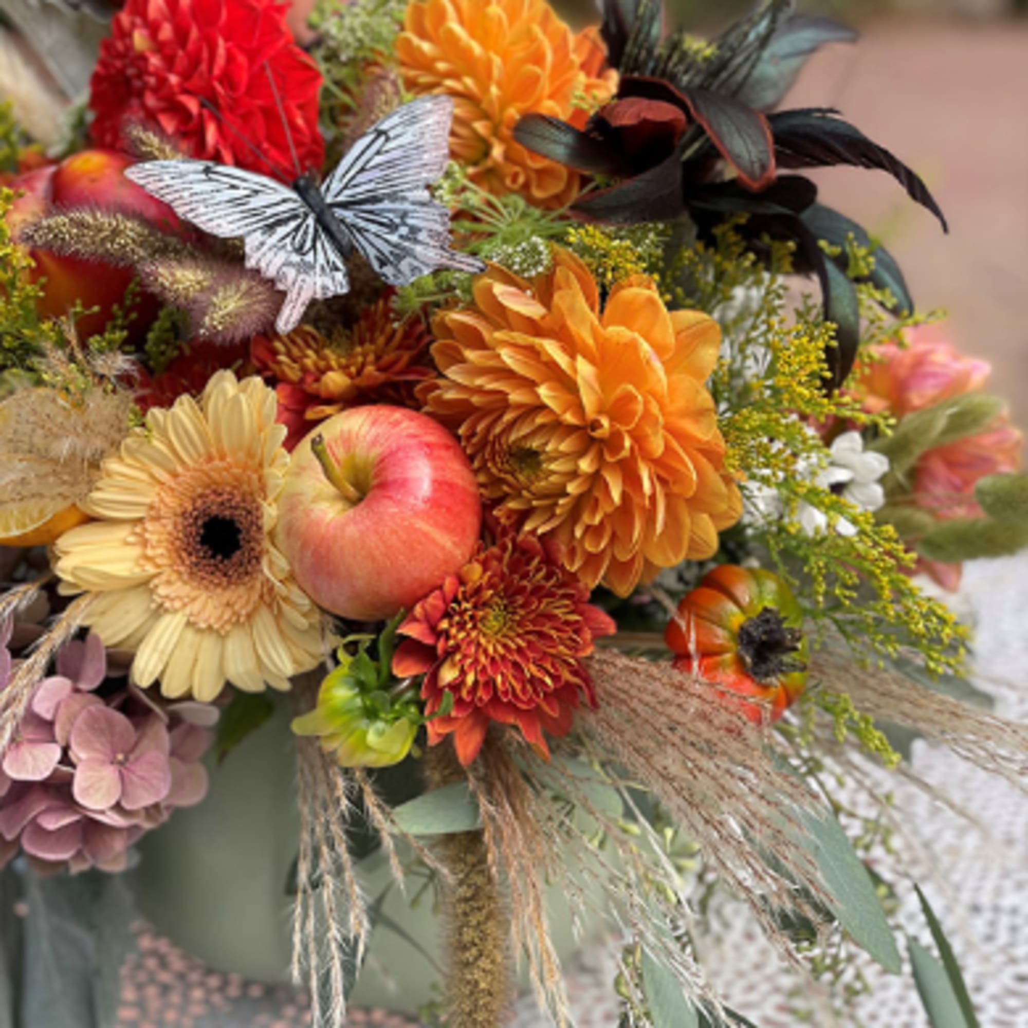 Autumn bouquet with orange and red flowers, apples, and a butterfly decoration