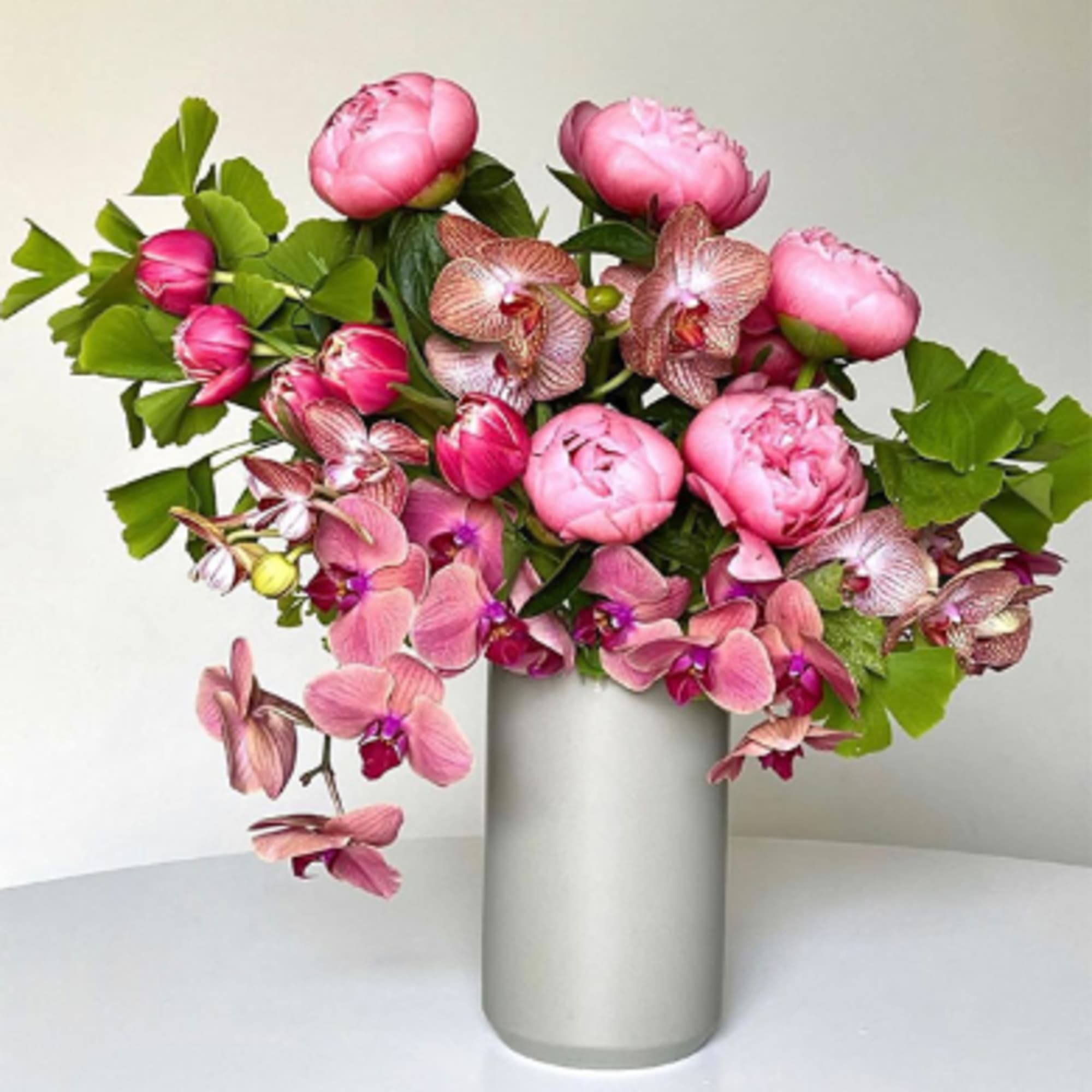 Pink peonies and orchids arranged in a tall silver vase