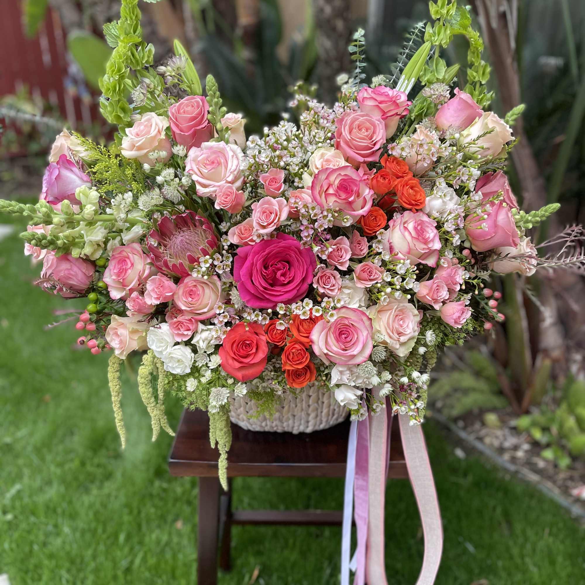 Large bouquet of pink and coral roses in a woven basket with ribbon tails