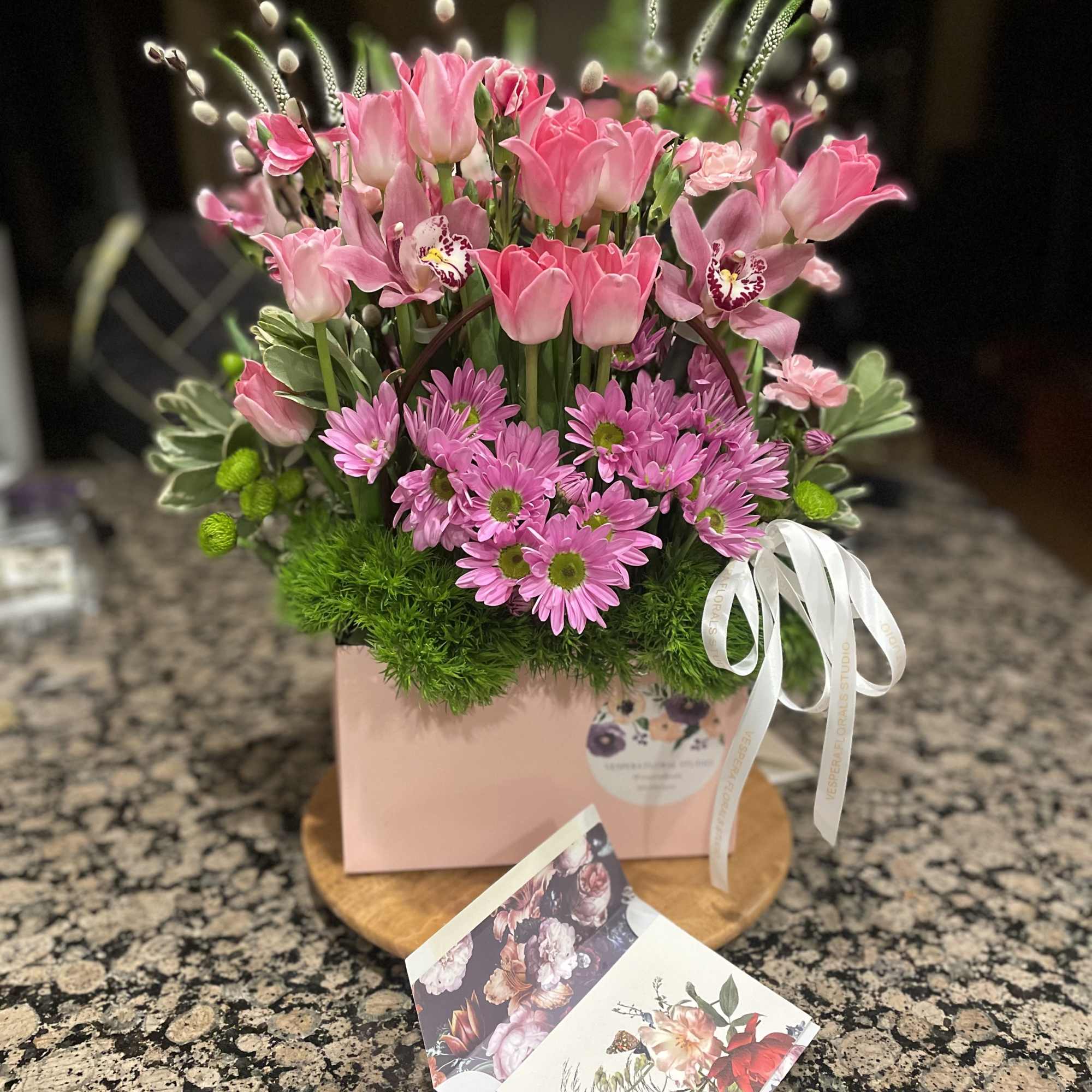 Pink tulips and daisies arranged in a pink box with a white ribbon