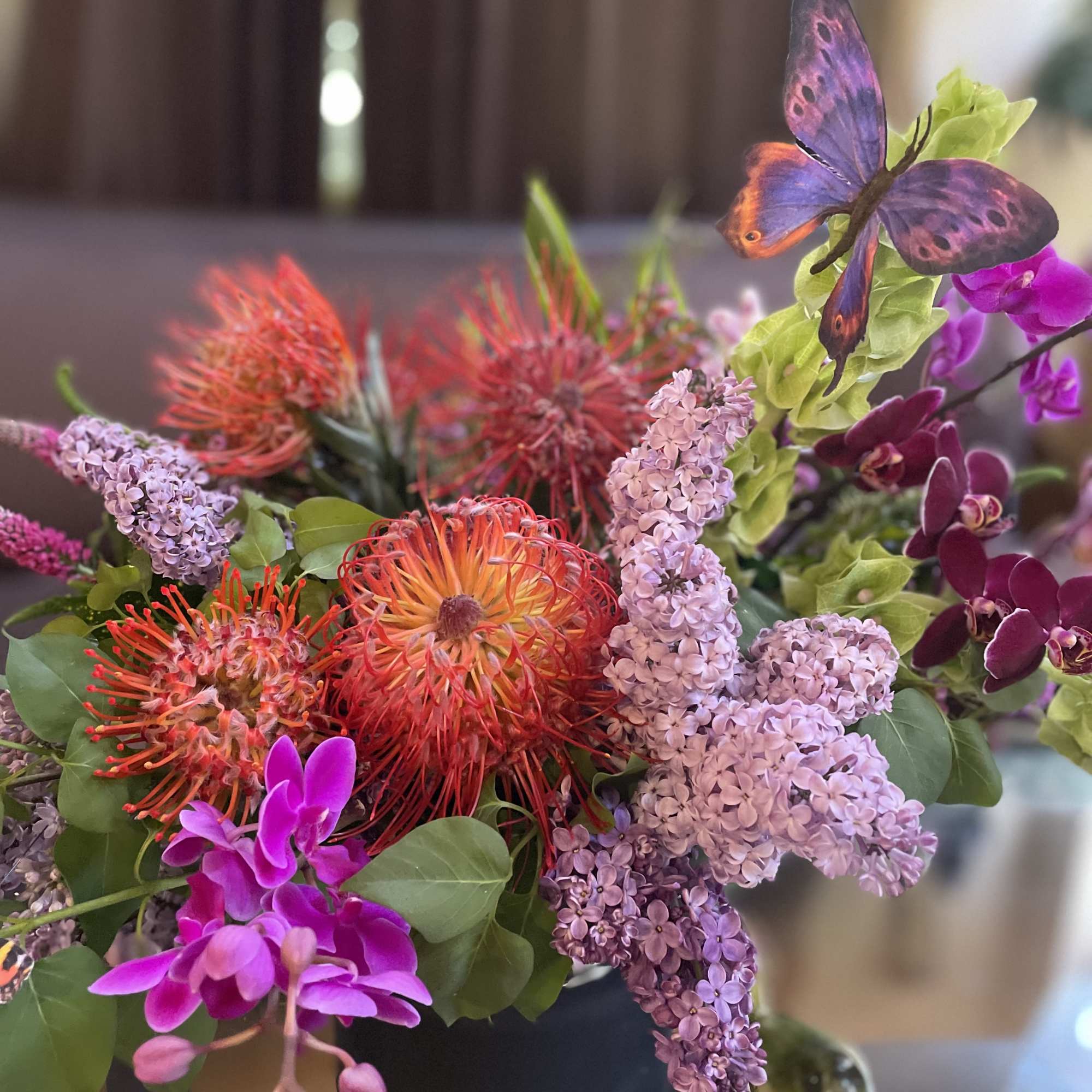 Colorful bouquet with orange pincushion blooms, lilac clusters, and purple orchids