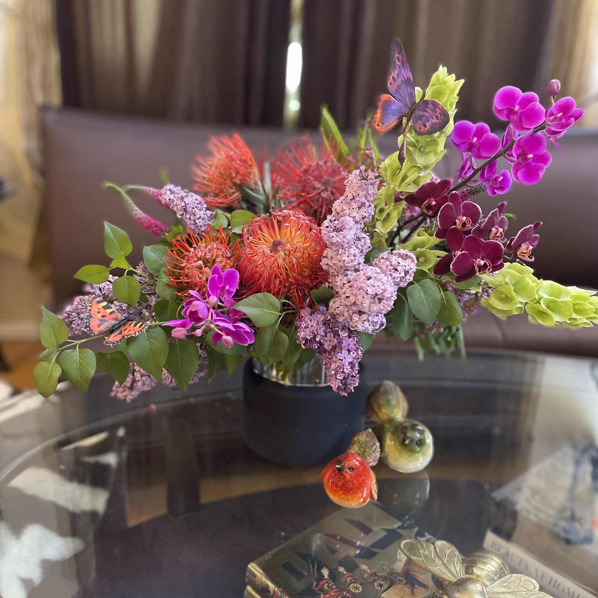 Colorful floral arrangement in a black vase with orchids and orange blooms