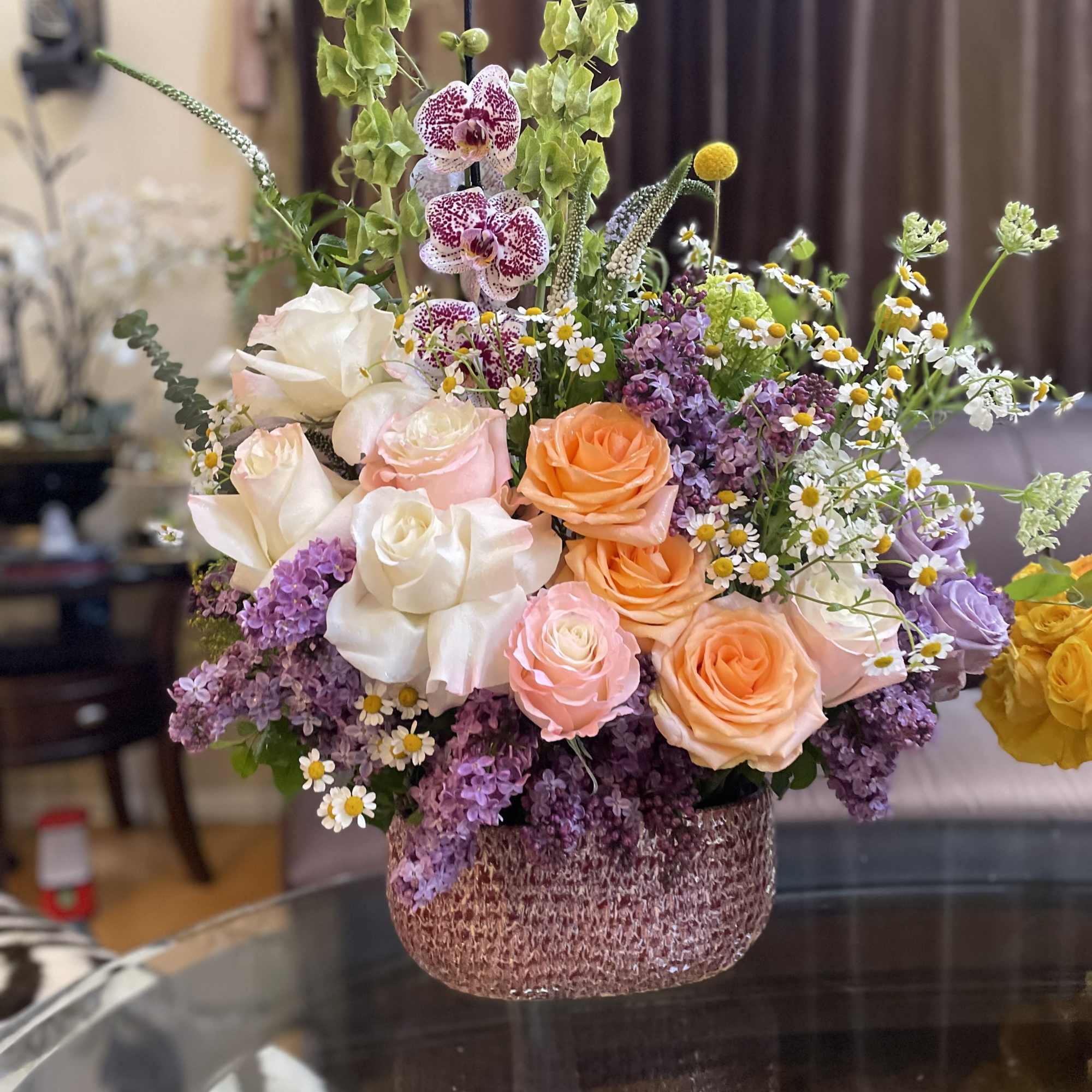 Mixed bouquet of roses, orchids, and small daisies in a textured vase