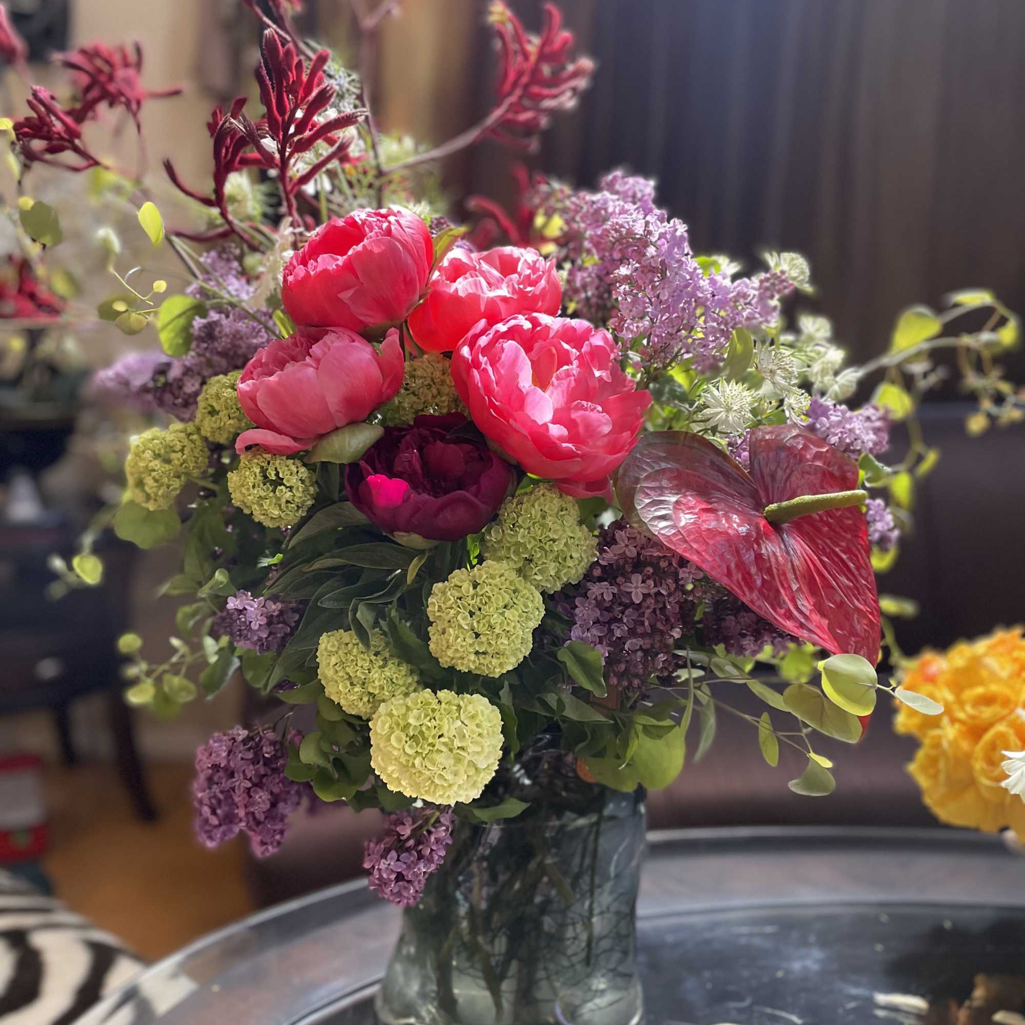 Pink peonies and purple flowers arranged in a glass vase