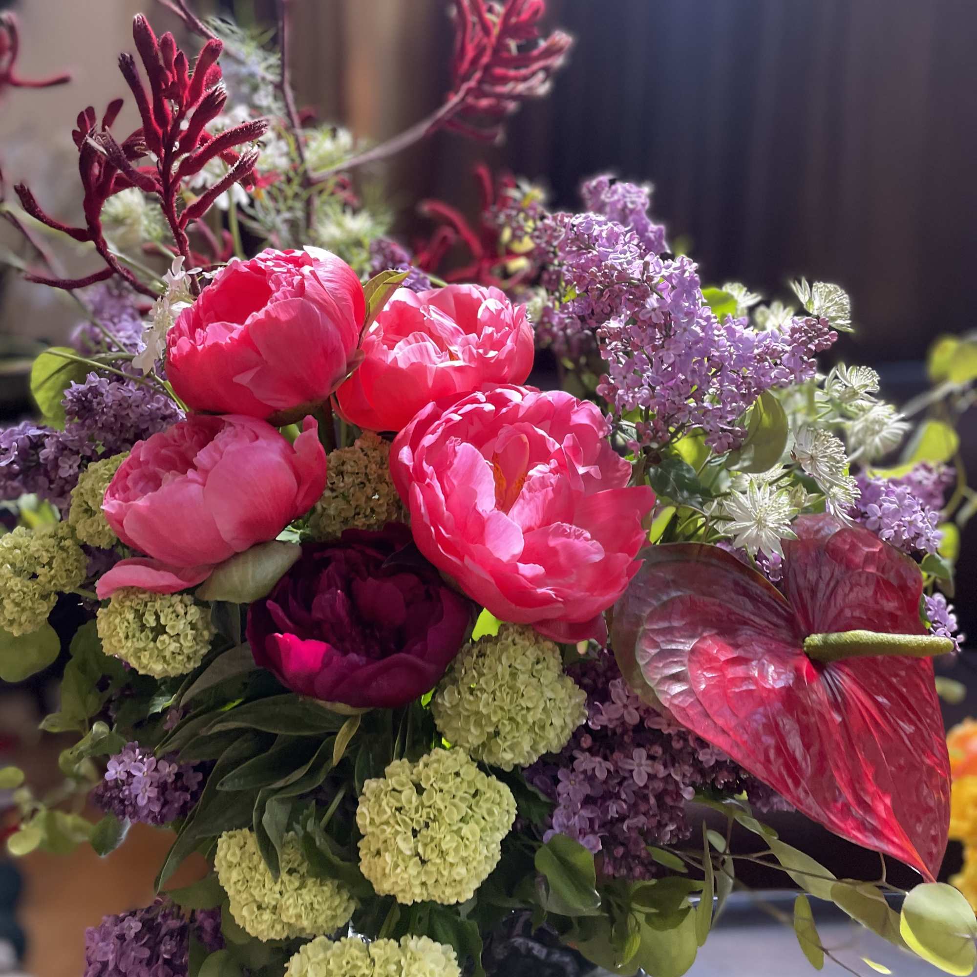 Pink peonies and purple flowers in a vase with a red anthurium