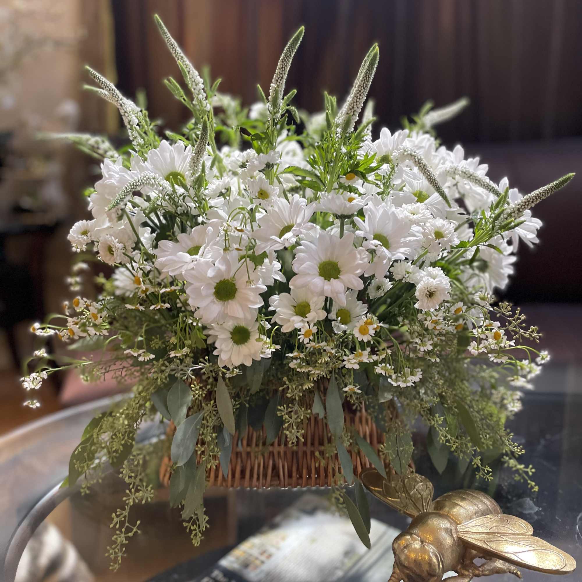 White daisy bouquet in a wicker basket with trailing greenery