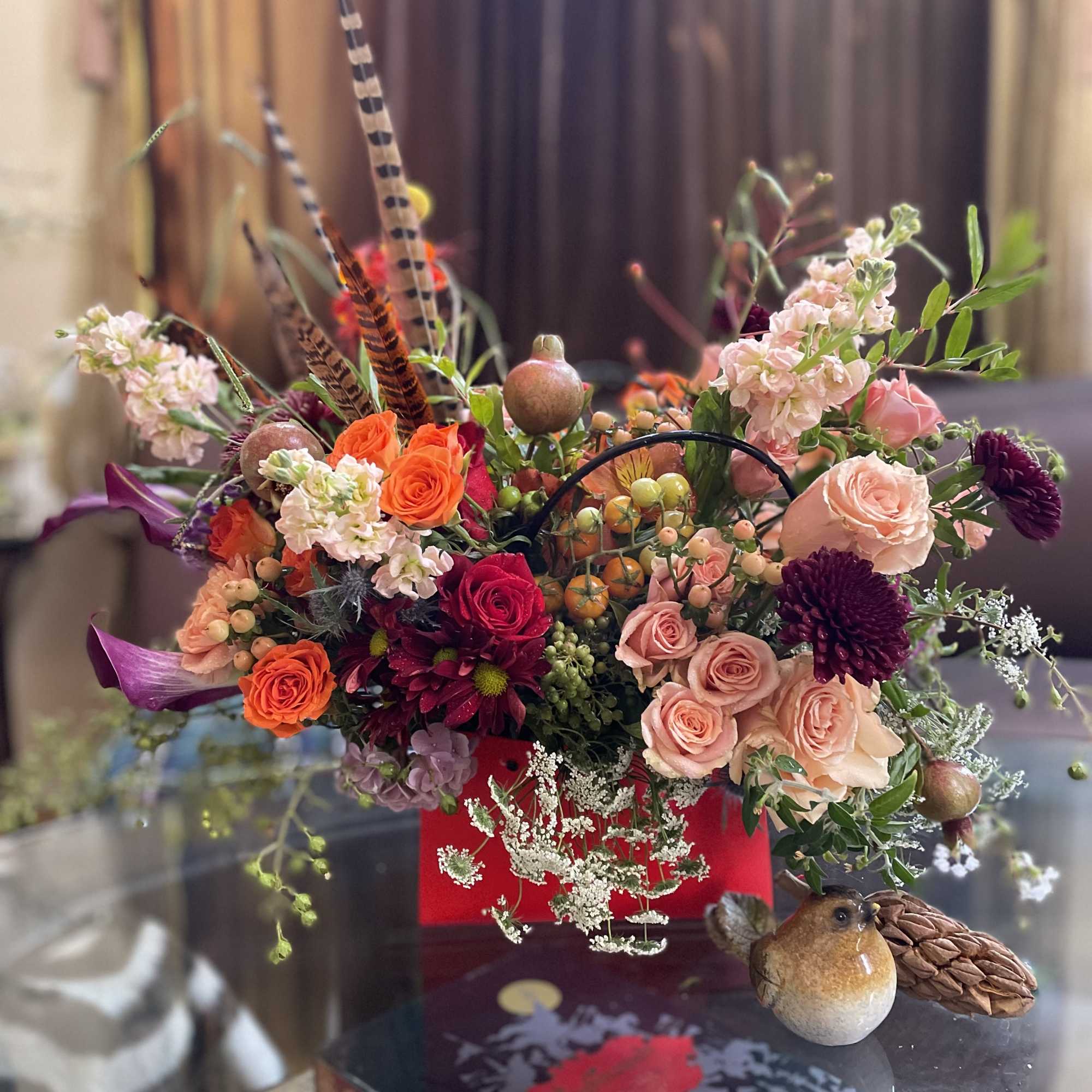 Mixed bouquet with roses, chrysanthemums, and decorative bird accents in a red container