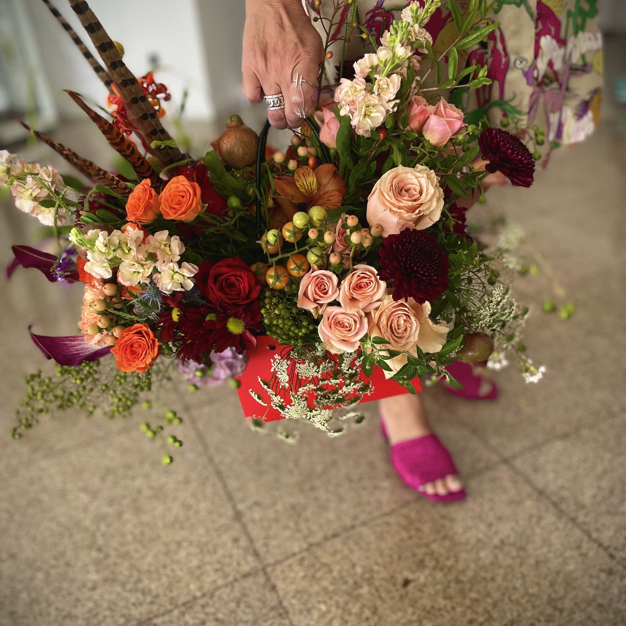 Handheld bouquet of mixed roses and orange blooms with decorative feathers