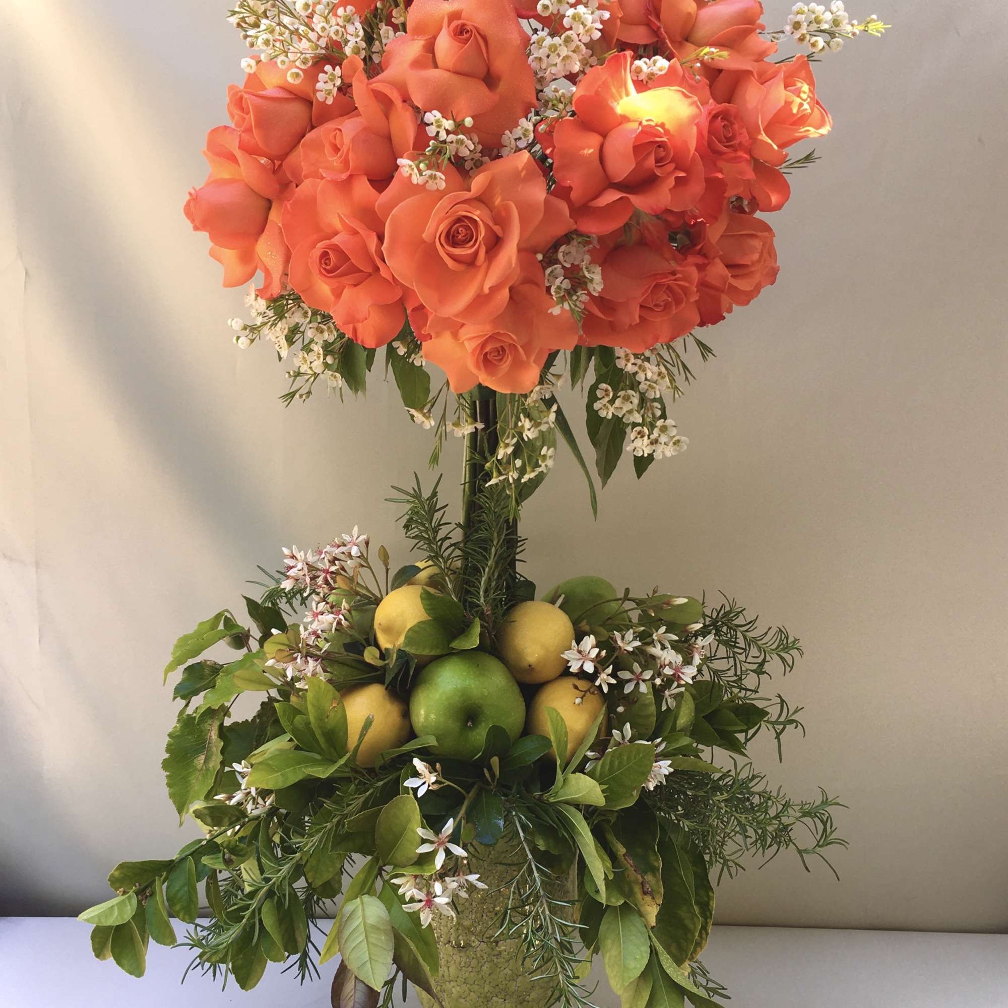 Orange roses in a tall vase with lemons and greenery
