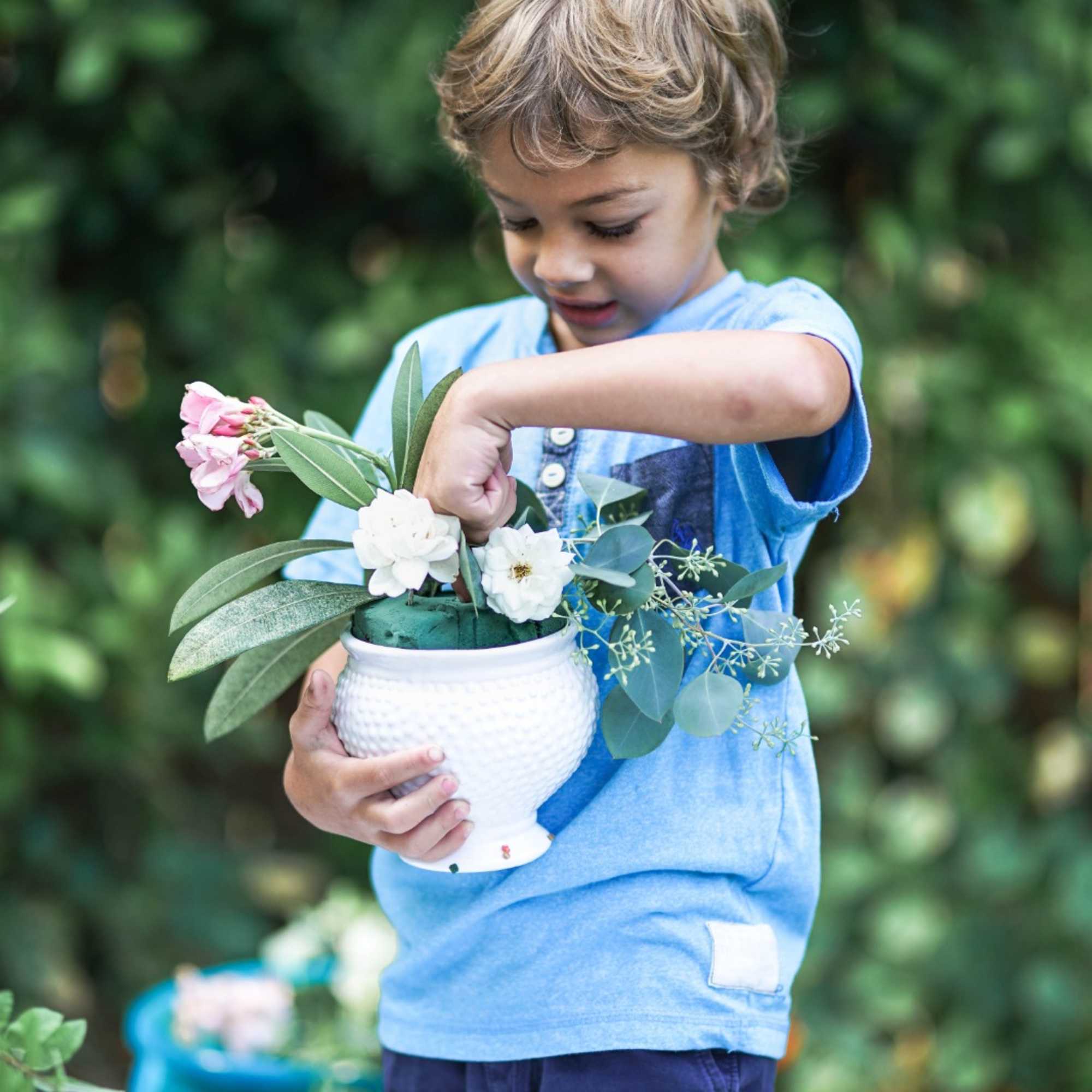 Child holding a white vase with pink and white flowers