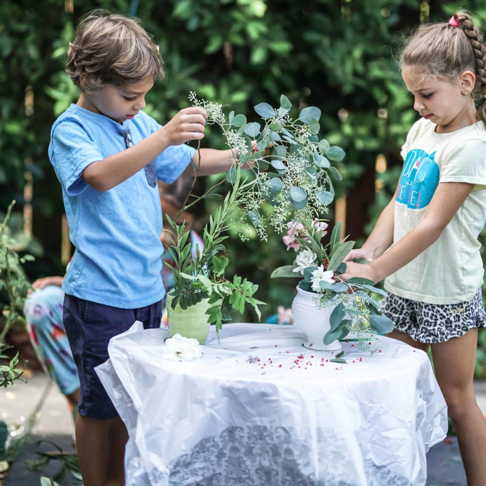 Two children arranging greenery and small flowers in vases at a table