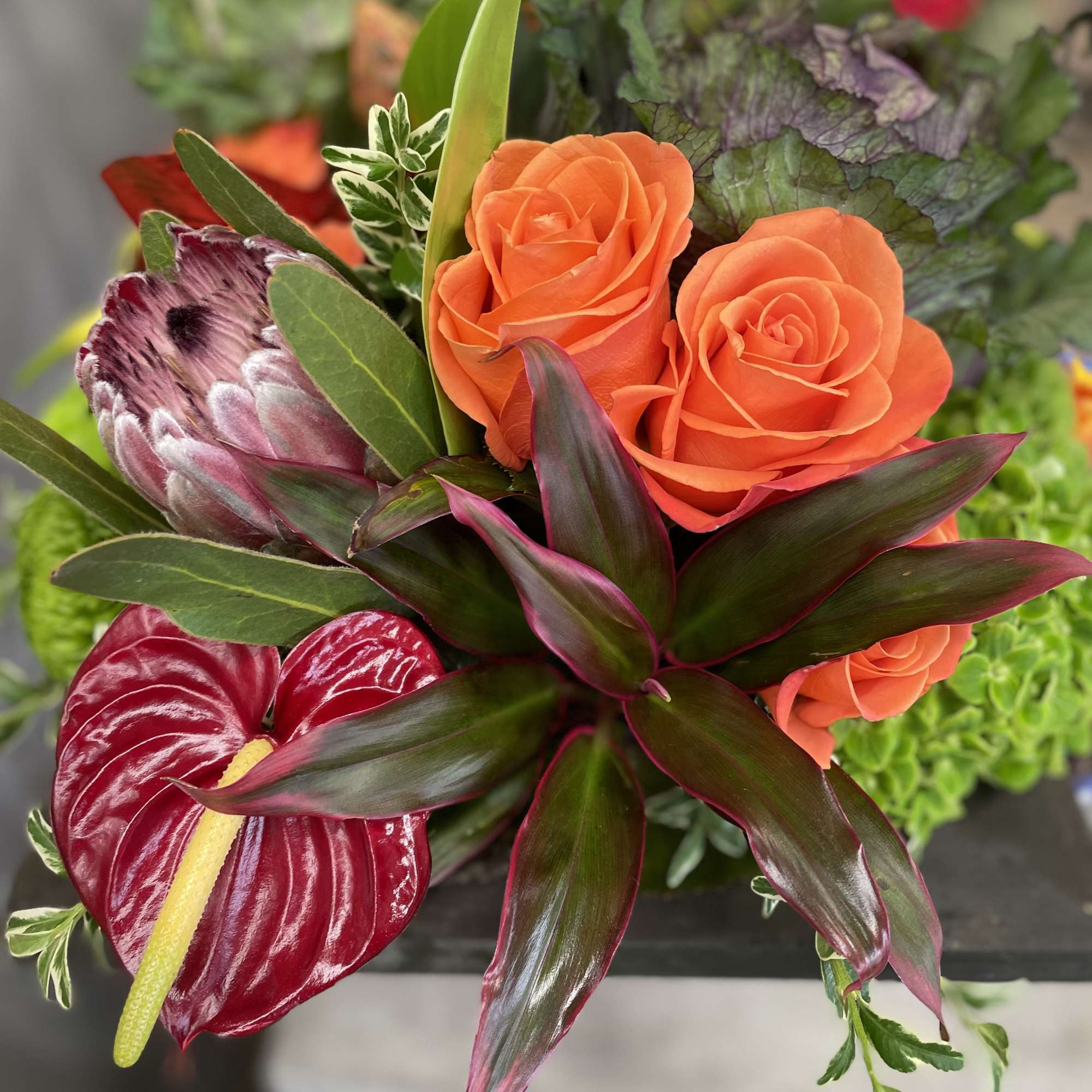 Orange roses with tropical foliage and a red anthurium bloom
