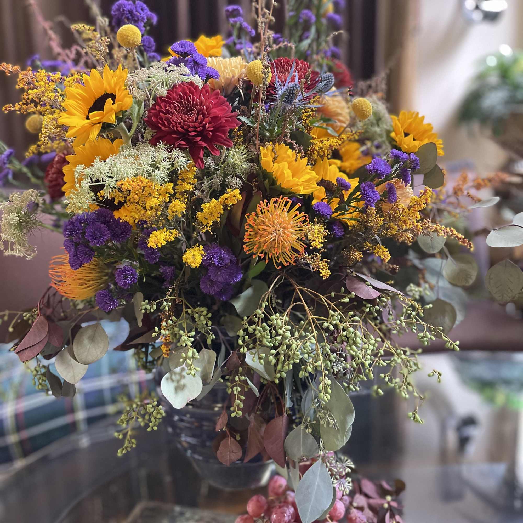 Mixed bouquet with sunflowers, chrysanthemums, and purple filler flowers in a glass vase