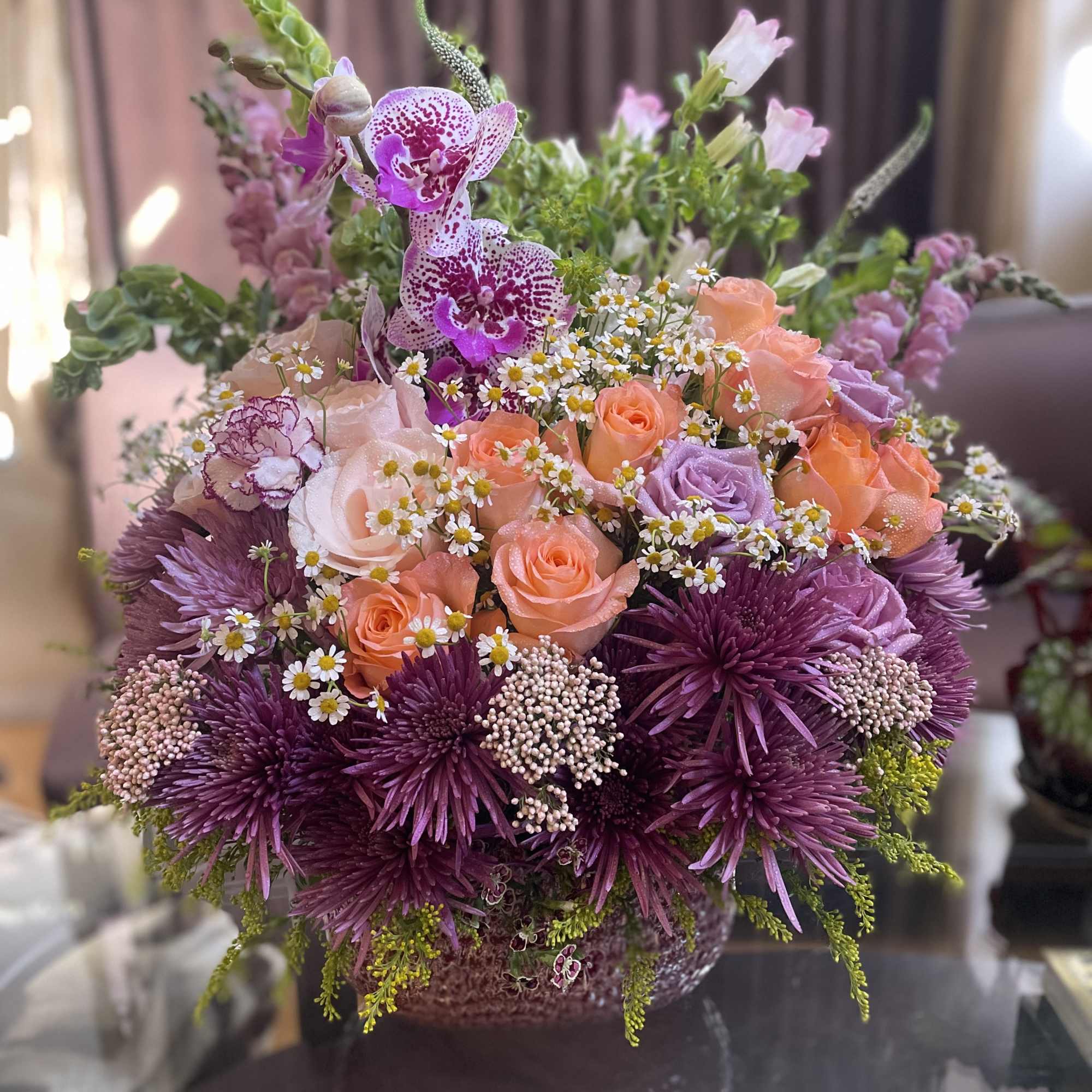 Mixed bouquet of peach and purple flowers in a low container