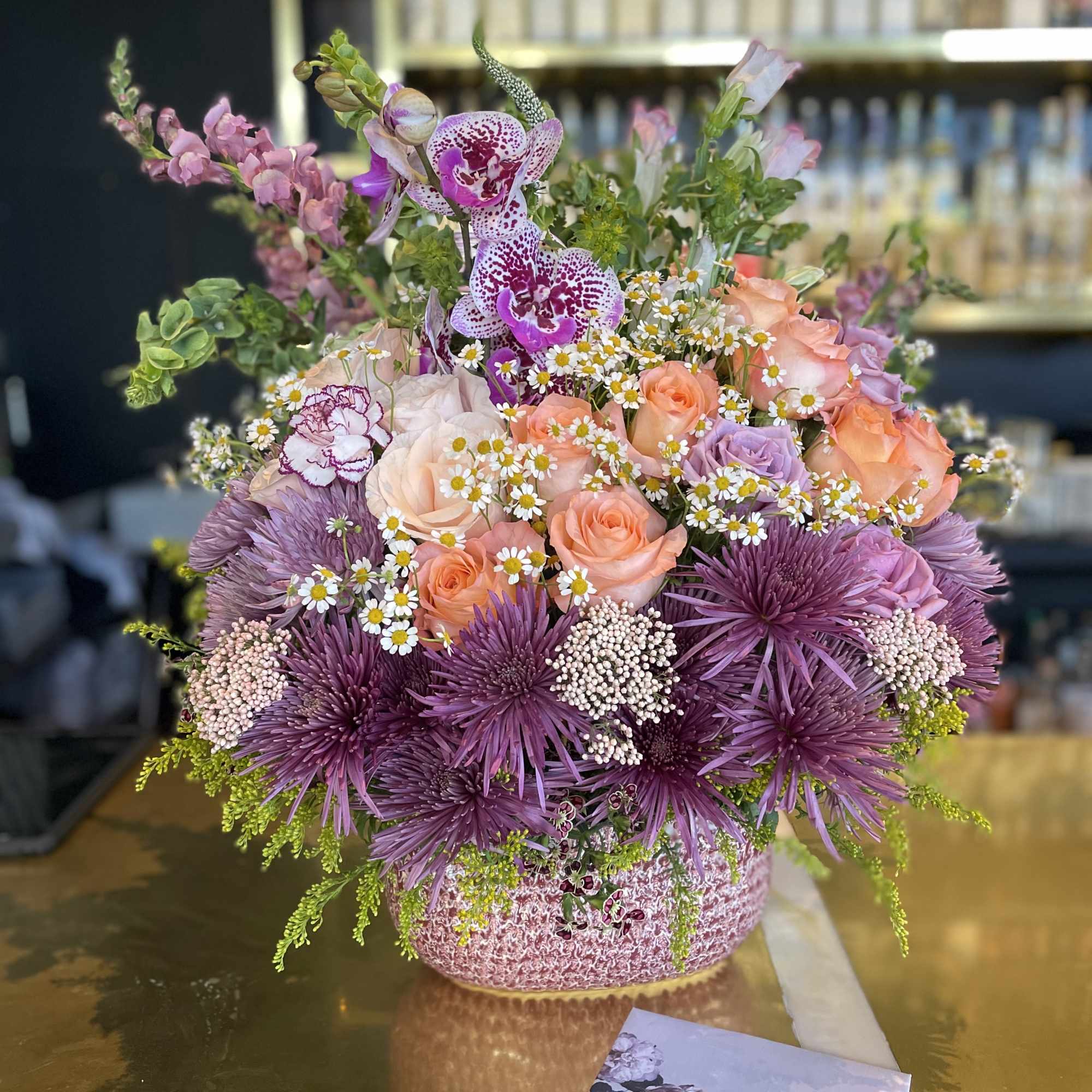 Mixed bouquet of pink, peach, and purple flowers in a textured vase