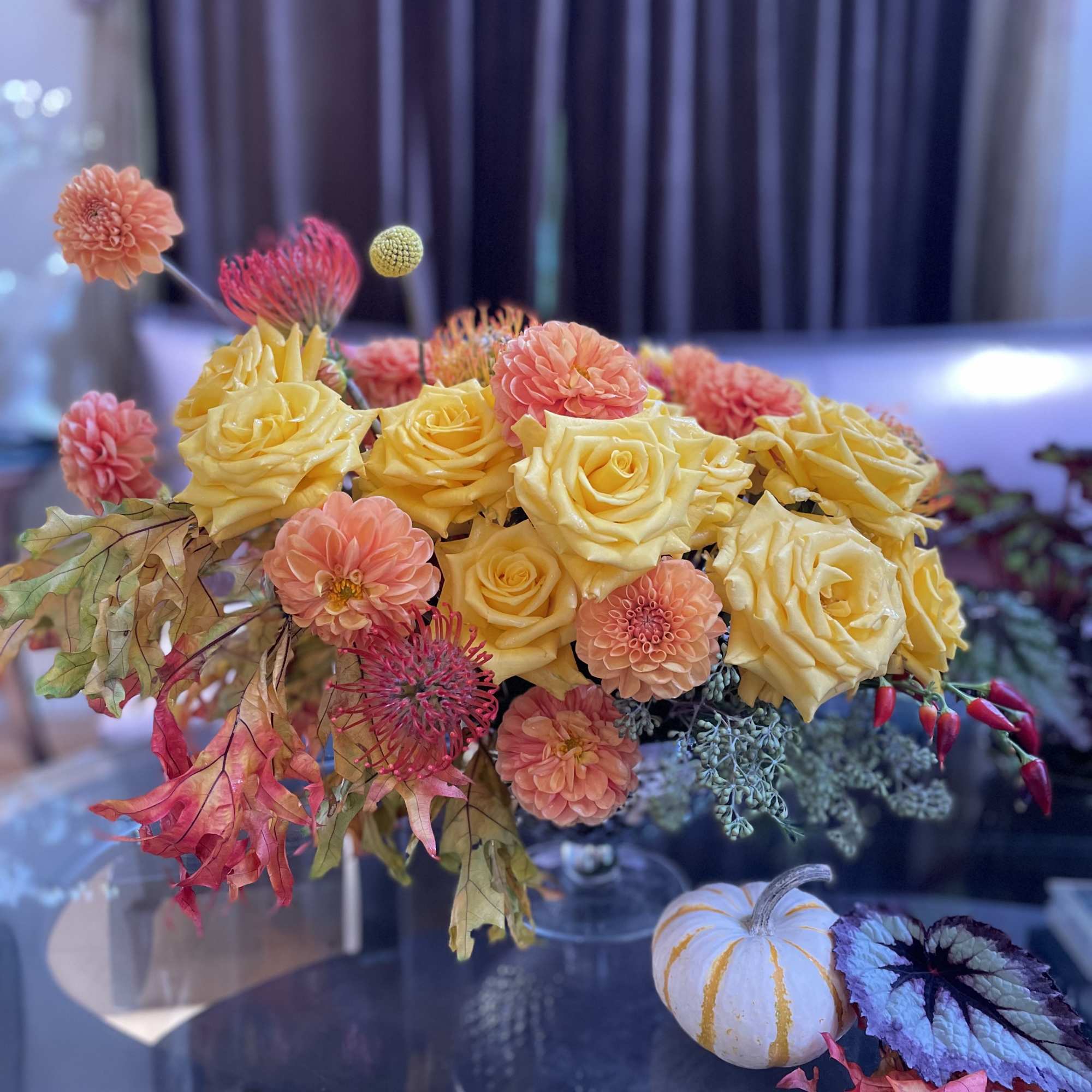 Yellow roses and peach dahlias in a low arrangement with autumn leaves
